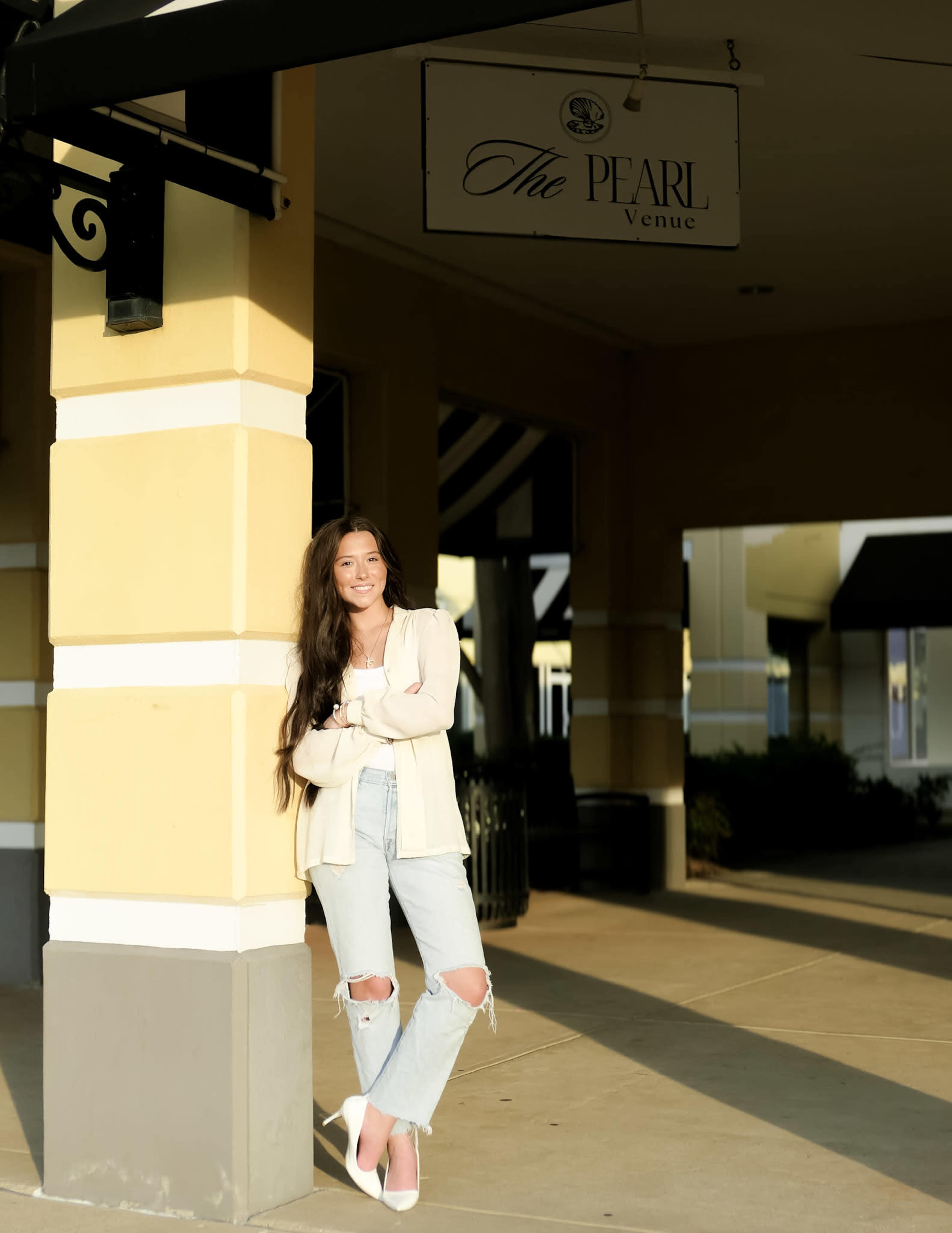 A woman with long hair leans against a yellow column near a sign for "The Pearl Venue."