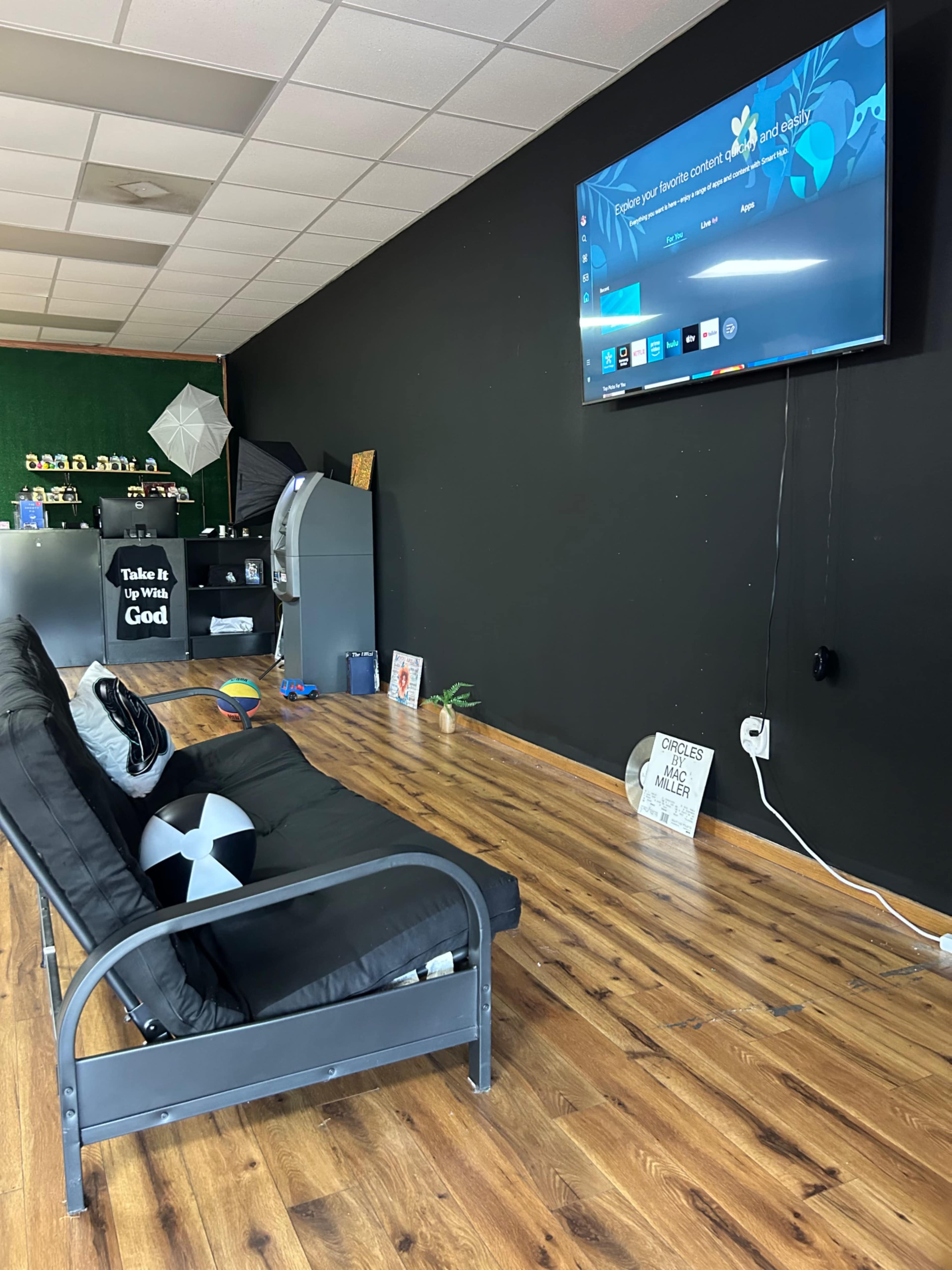 The image shows a modern interior space with a black wall, a television mounted on it, a sofa with a cushion, and various decor items in the background.