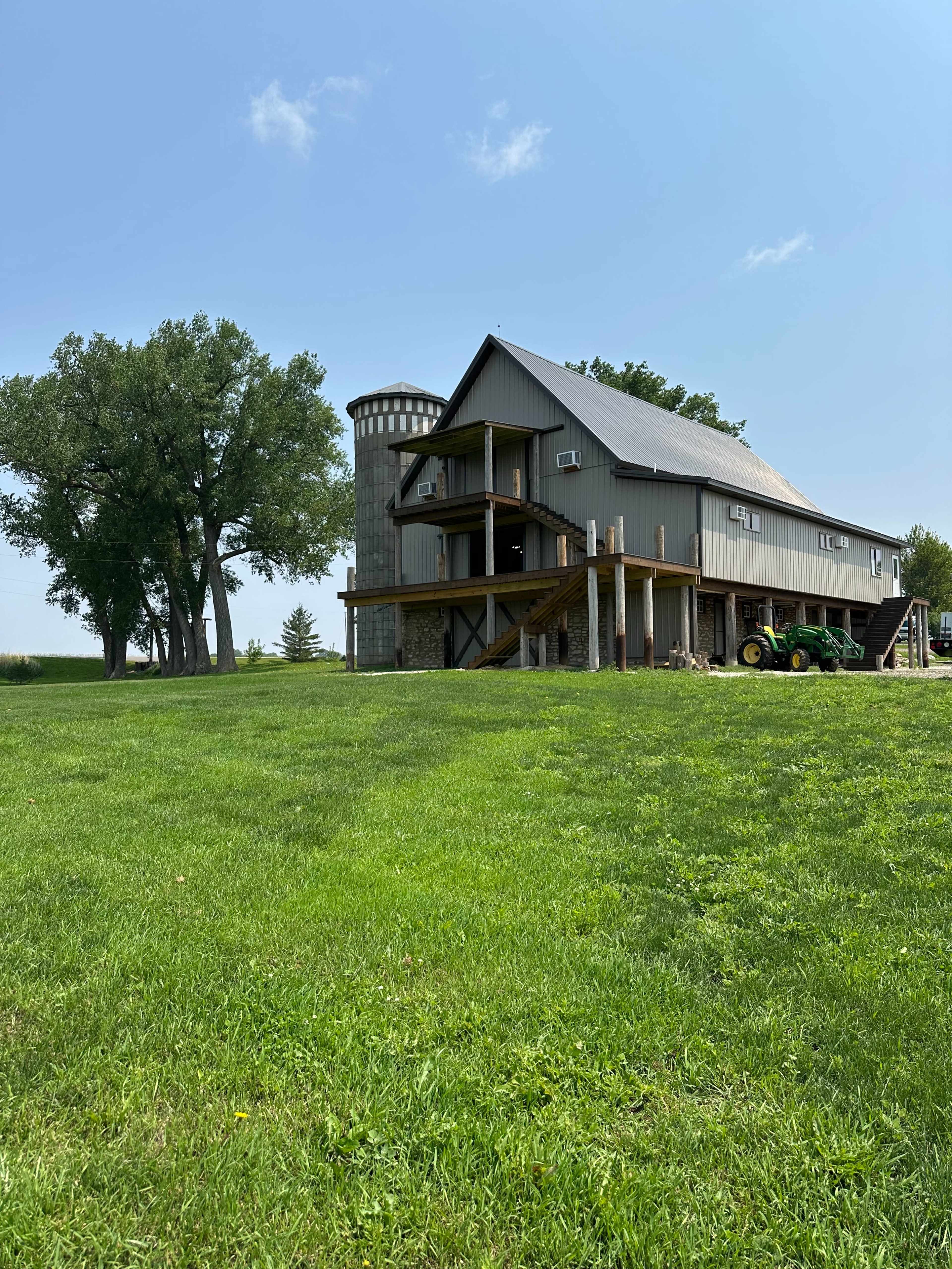 A two-story barn-style house with a silo is situated on a grassy field under a clear blue sky.