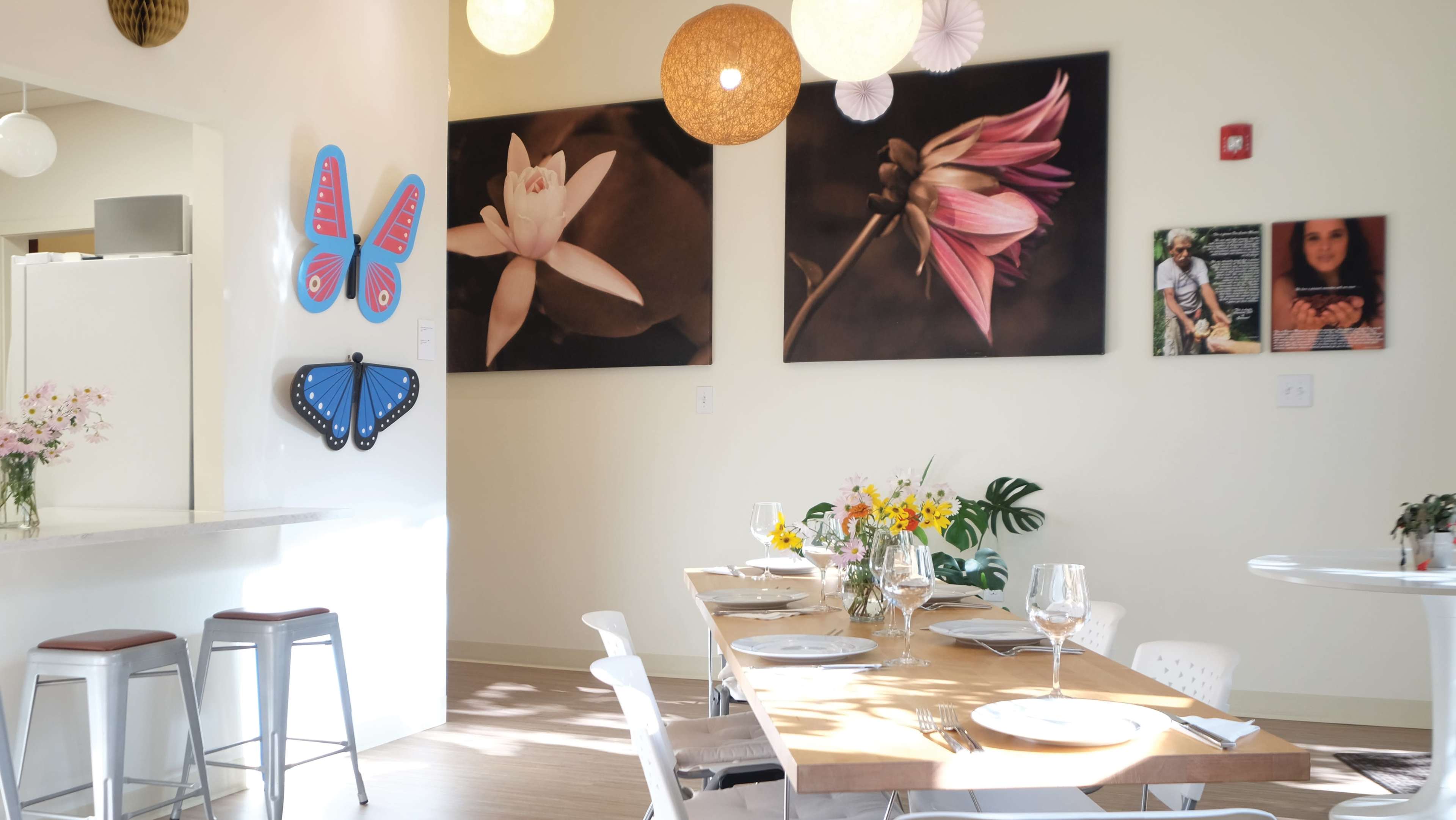 A bright dining area with a wooden table set for a meal, adorned with floral centerpieces, and large floral photographs on the walls.