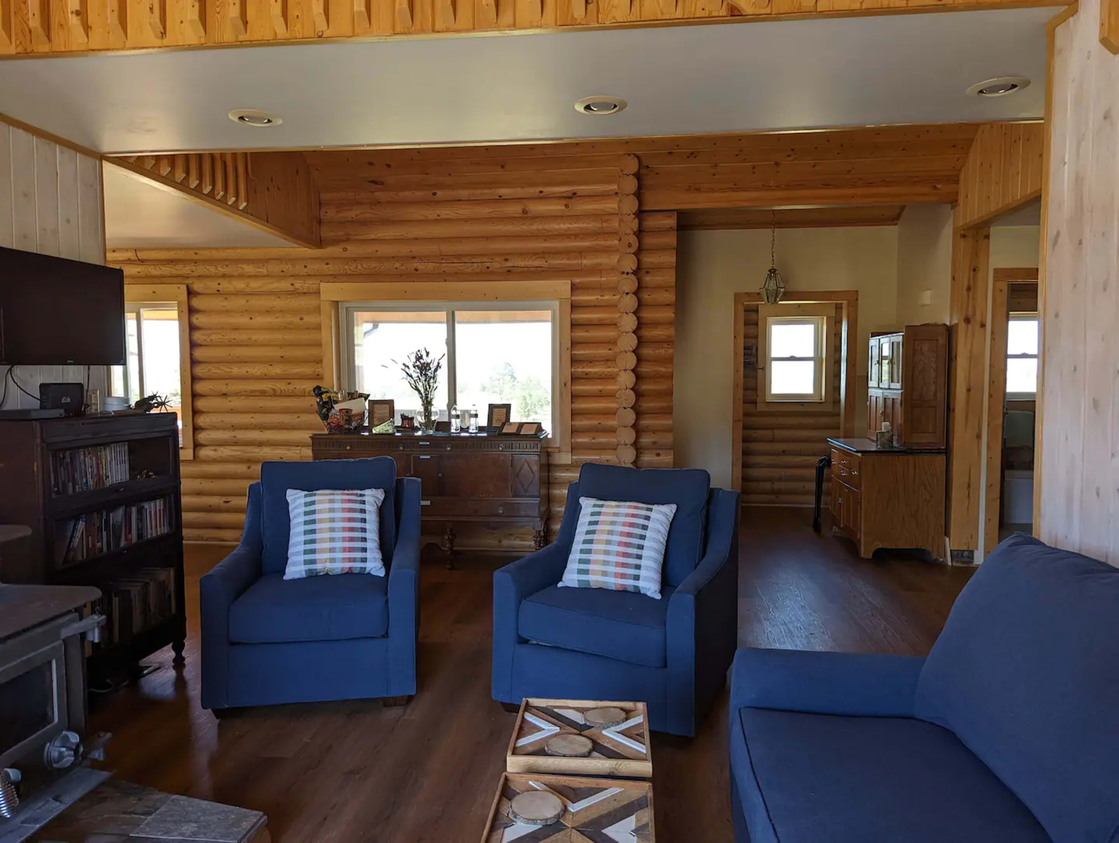 A cozy living room featuring blue armchairs, a wooden ceiling, and a large window with natural light.