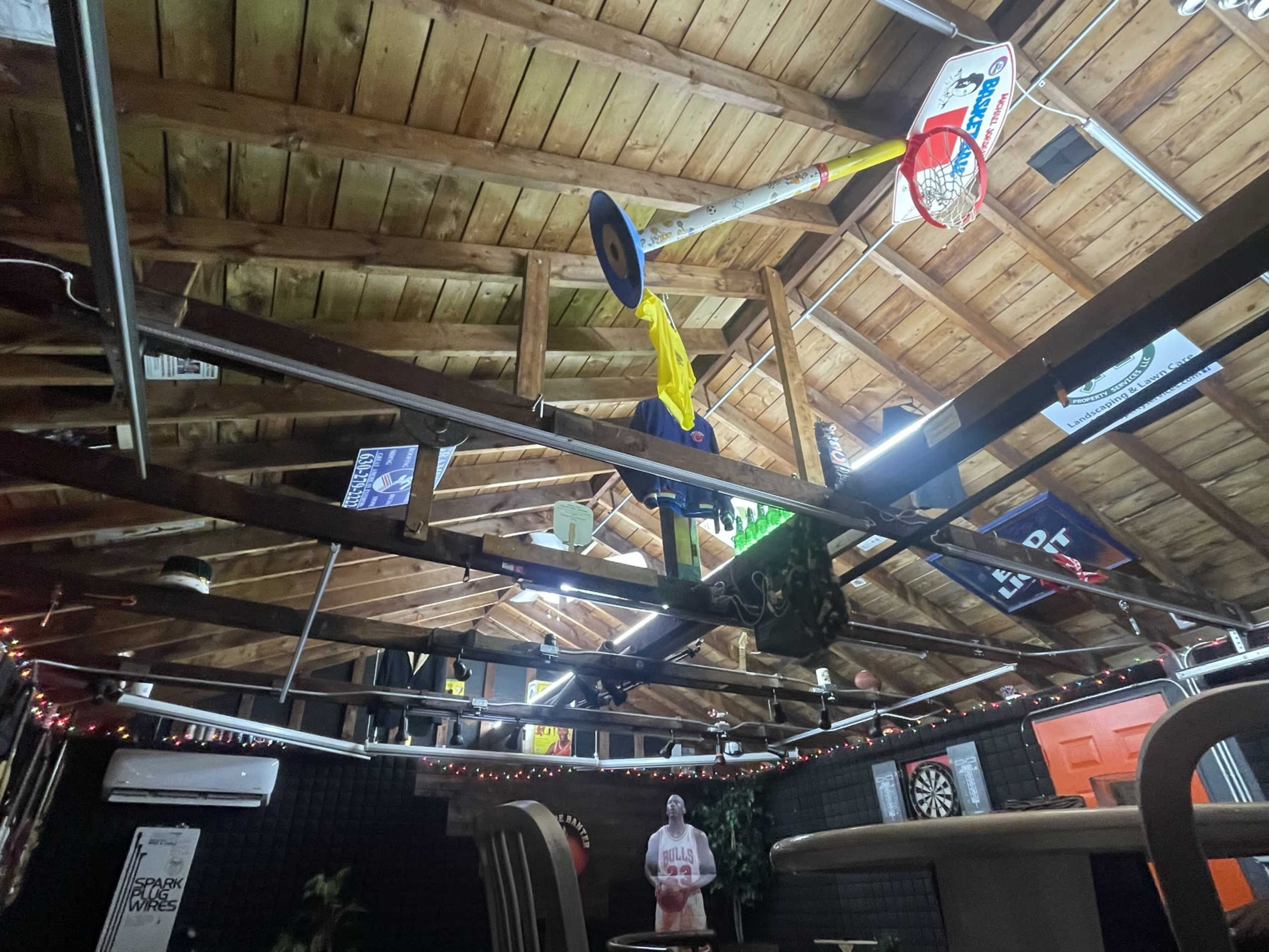 A rustic interior with a wooden ceiling adorned with sports memorabilia, lights, and a basketball hoop.