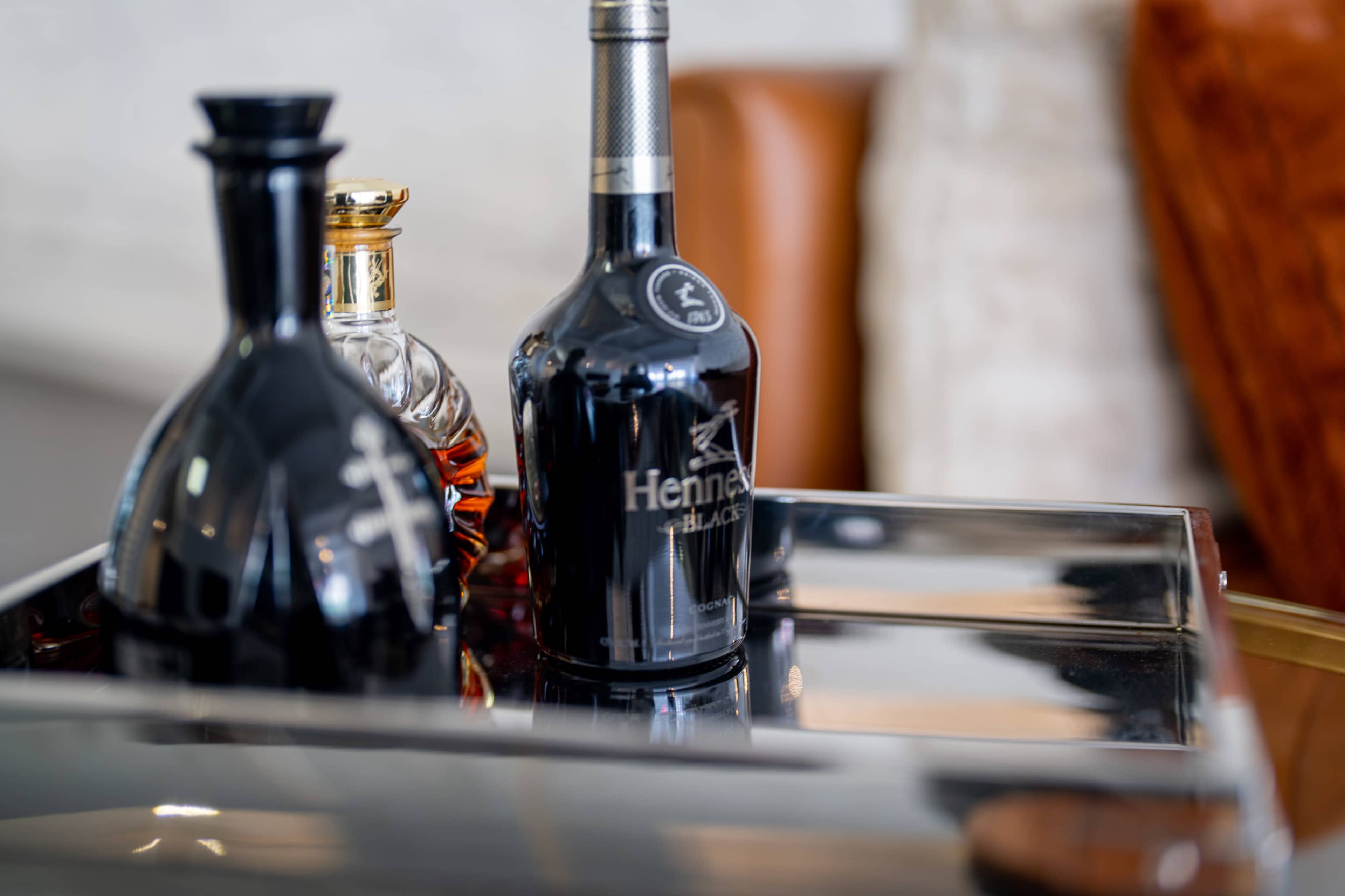 A black bottle of Hennessy is positioned next to a golden bottle on a reflective tray.