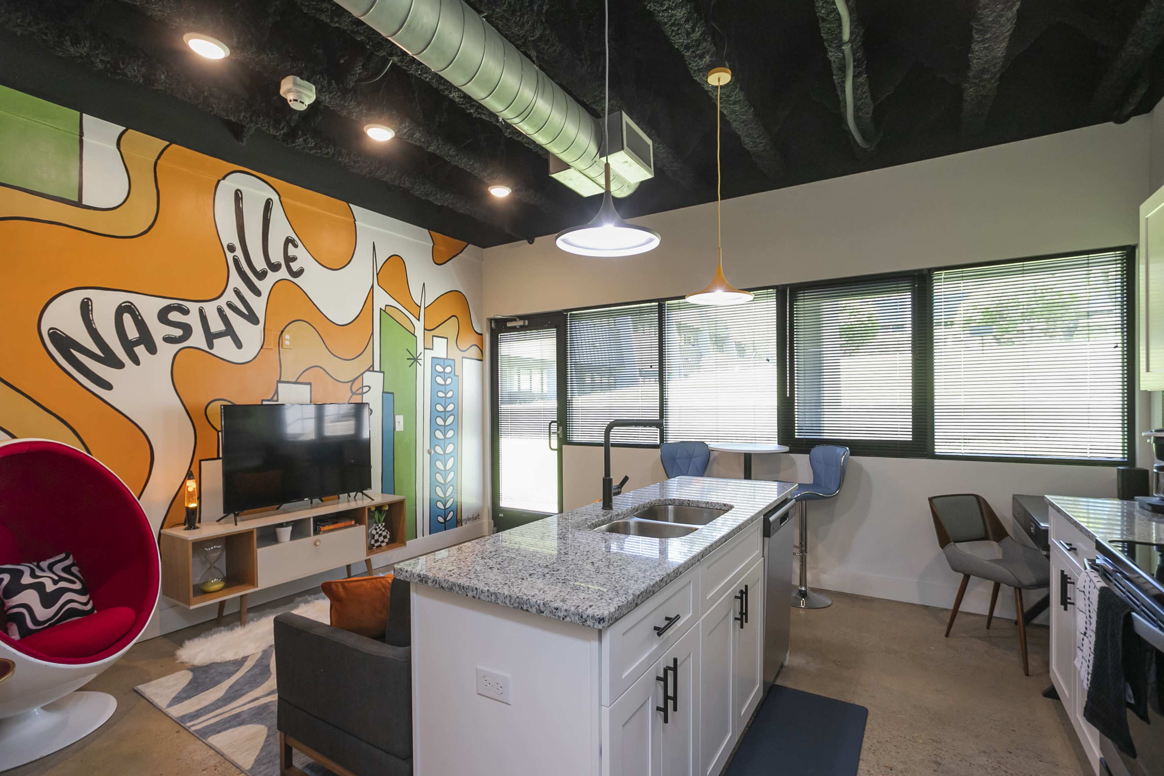 A modern kitchen and living area features a vibrant Nashville mural on the wall, with contemporary furnishings and large windows allowing natural light.