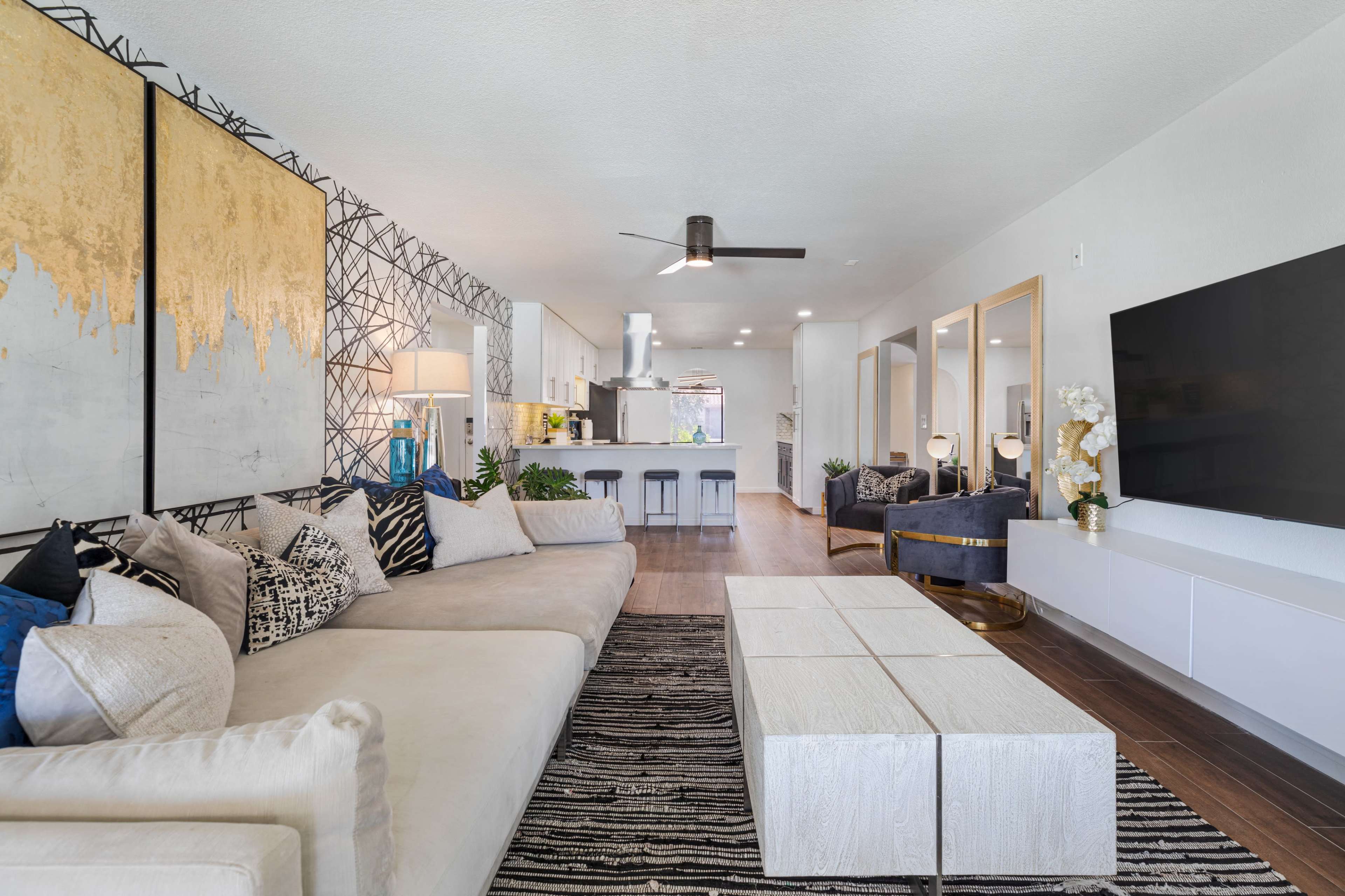 A modern living room features a sectional sofa, a striped area rug, and a sleek entertainment unit, with an open kitchen visible in the background.