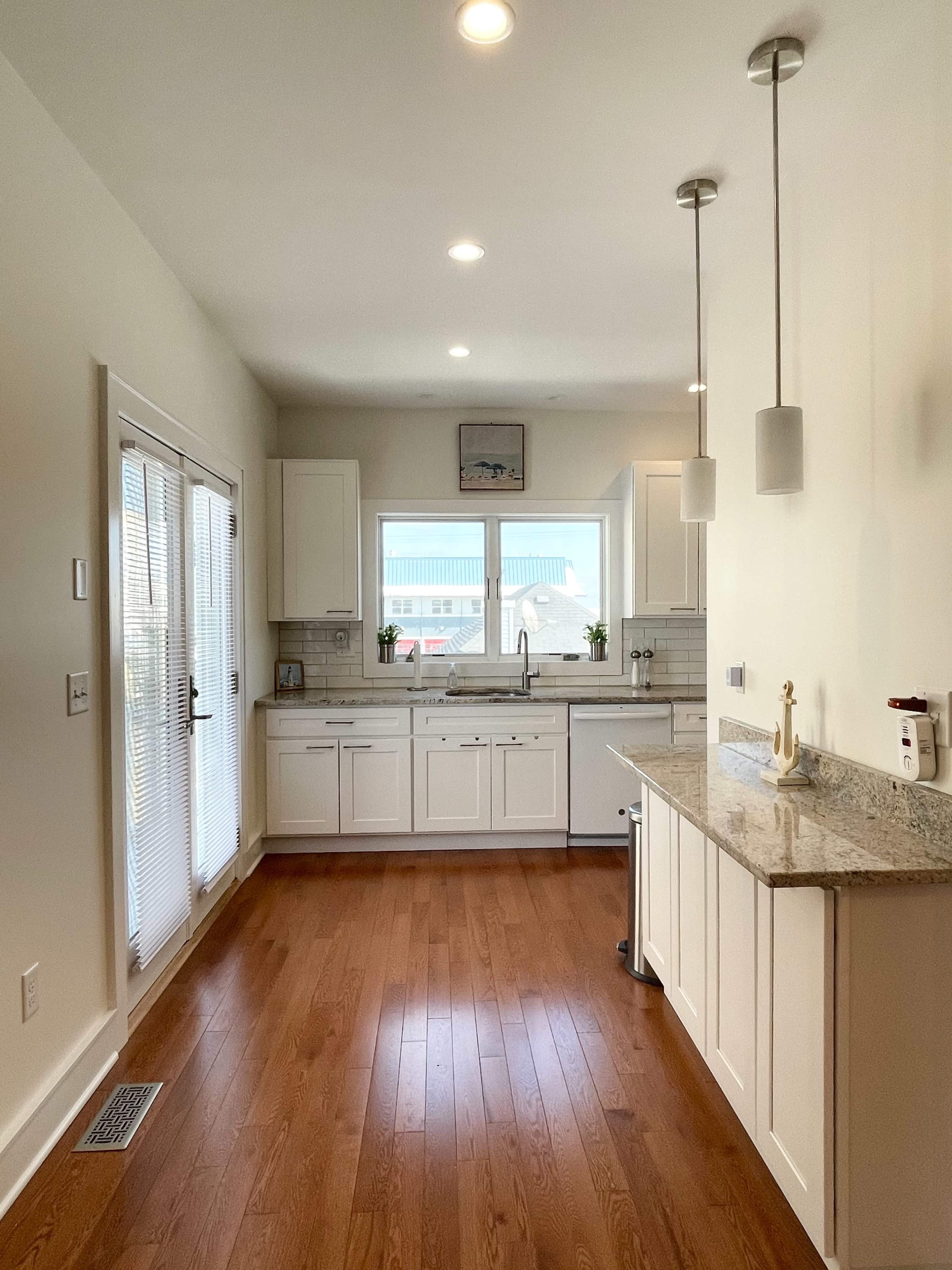 A modern kitchen features white cabinetry, a granite countertop, and a large window overlooking a patio area.