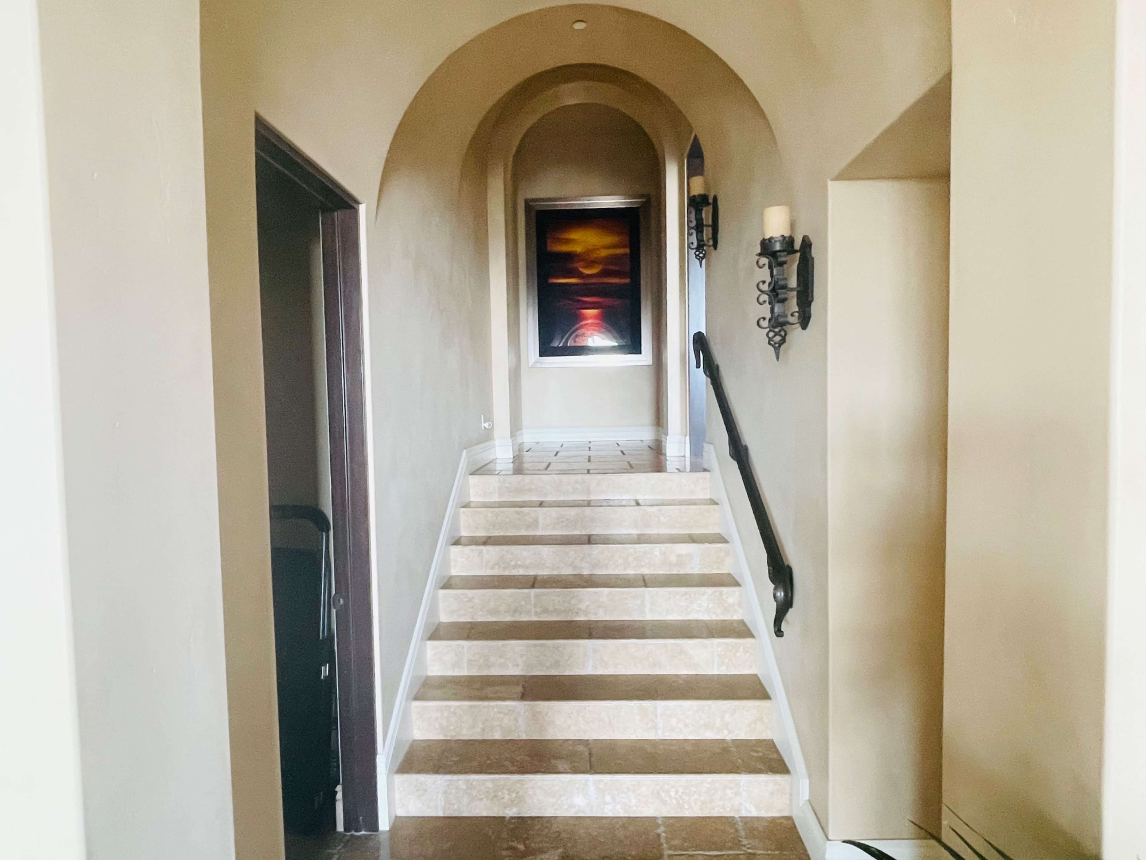 A stairway with stone steps leads up through an arched entry and features a large painting on the wall at the top.