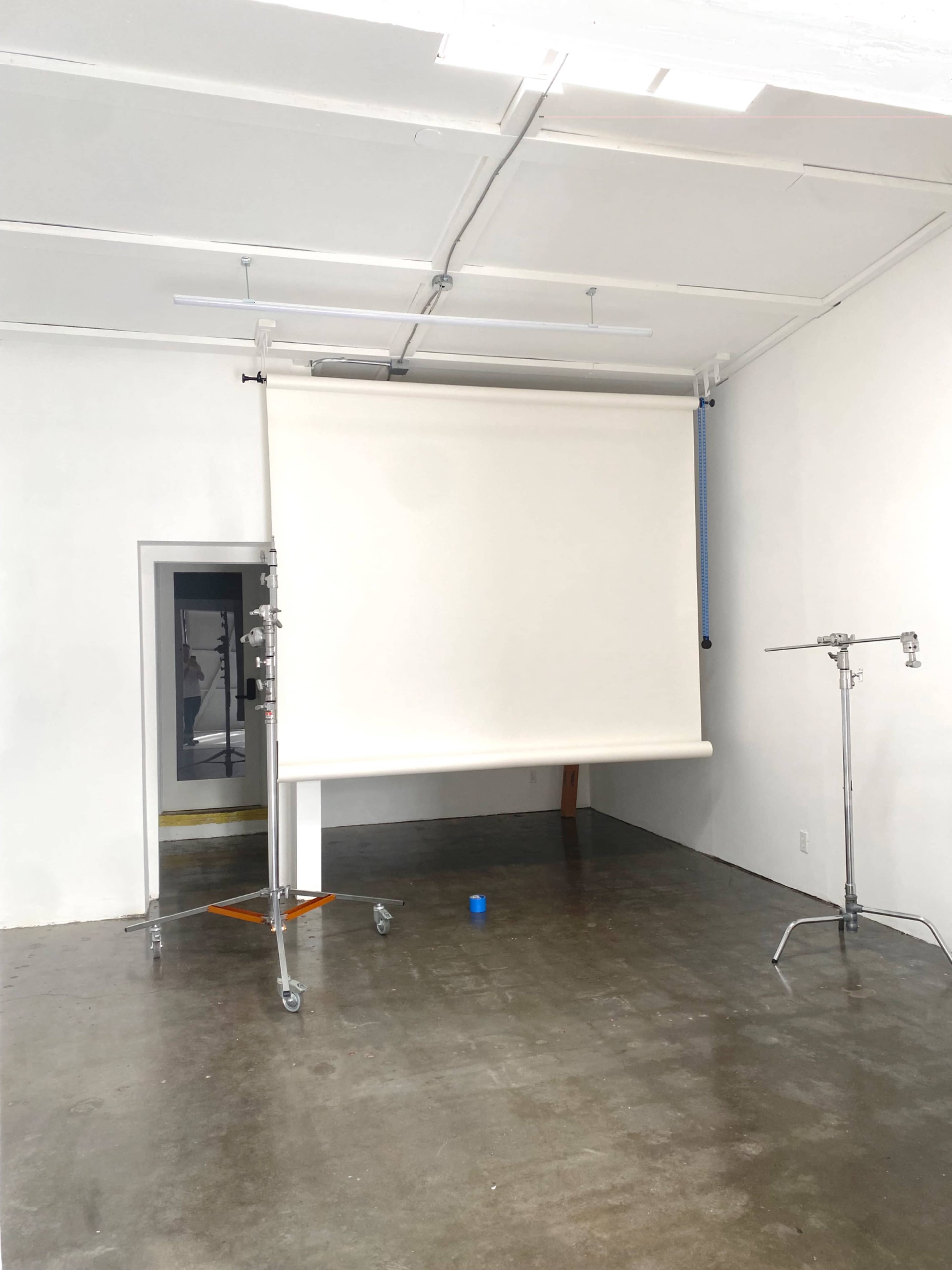 The image shows a spacious, empty room with a retractable white screen mounted on a stand and a single blue object on the floor.