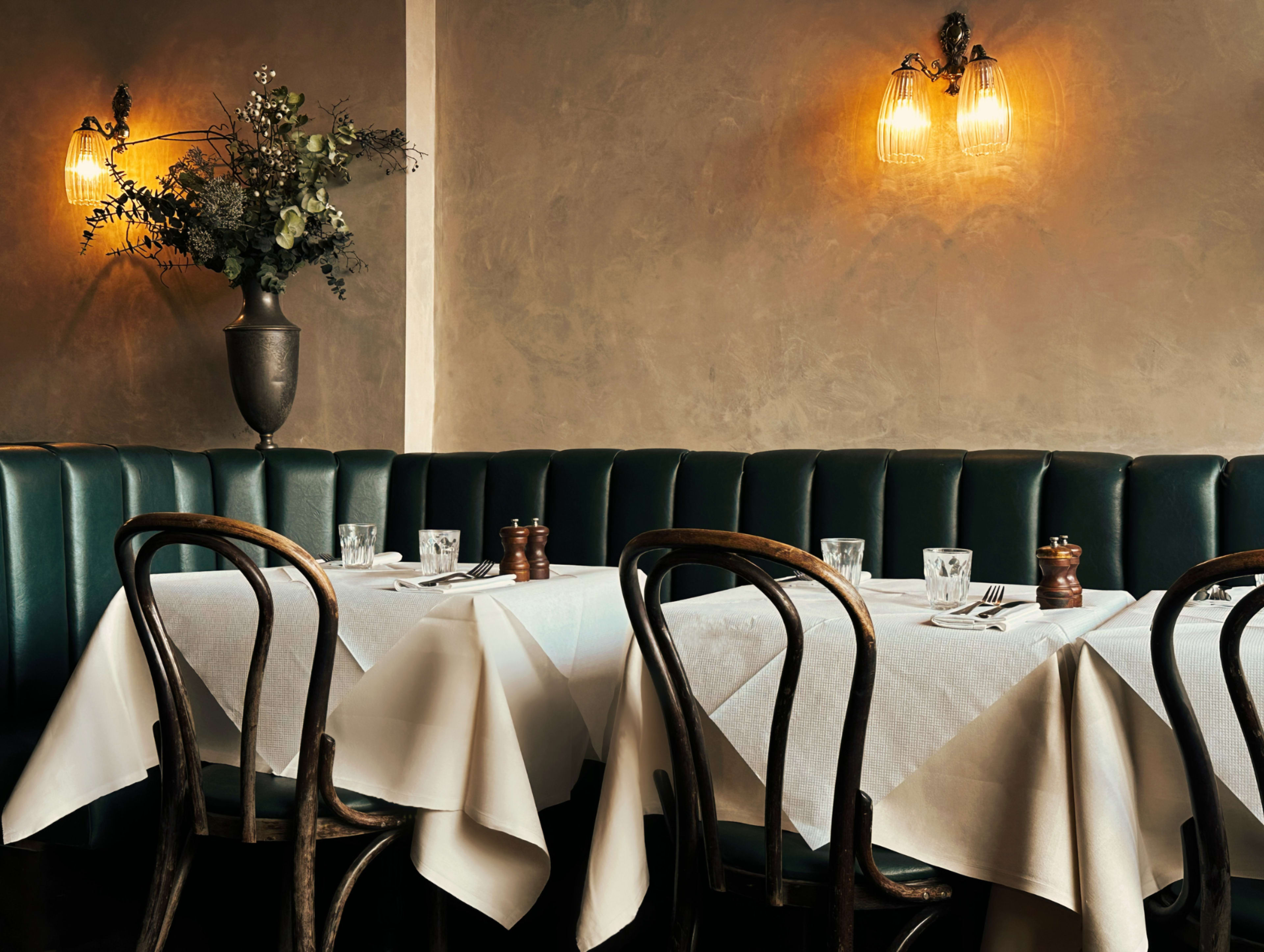 The image shows a restaurant interior with green upholstered seating, white tablecloths, and warm wall lighting.