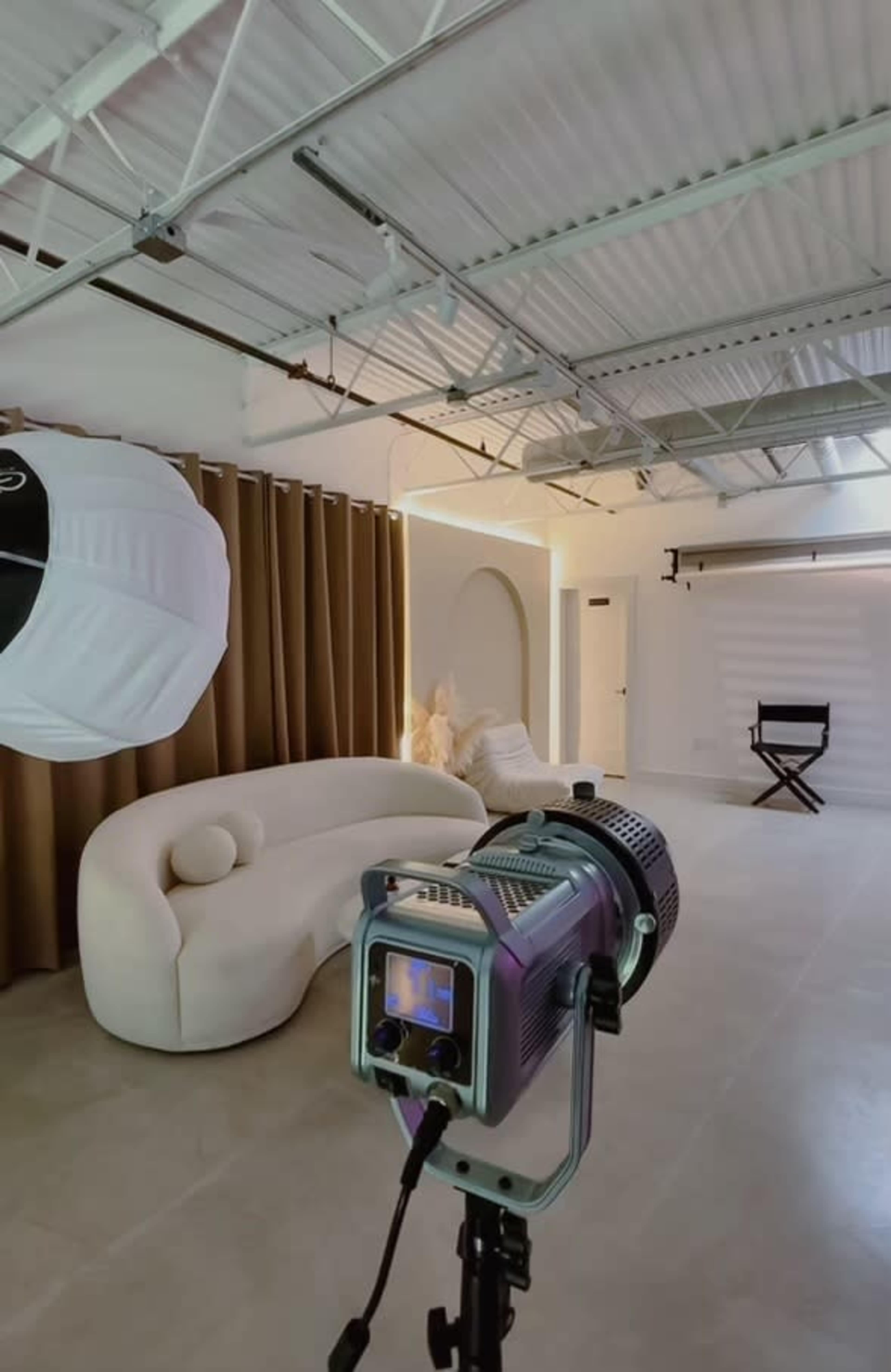 A photography studio with a soft white sofa, brown curtains, and a backdrop set up for shooting.