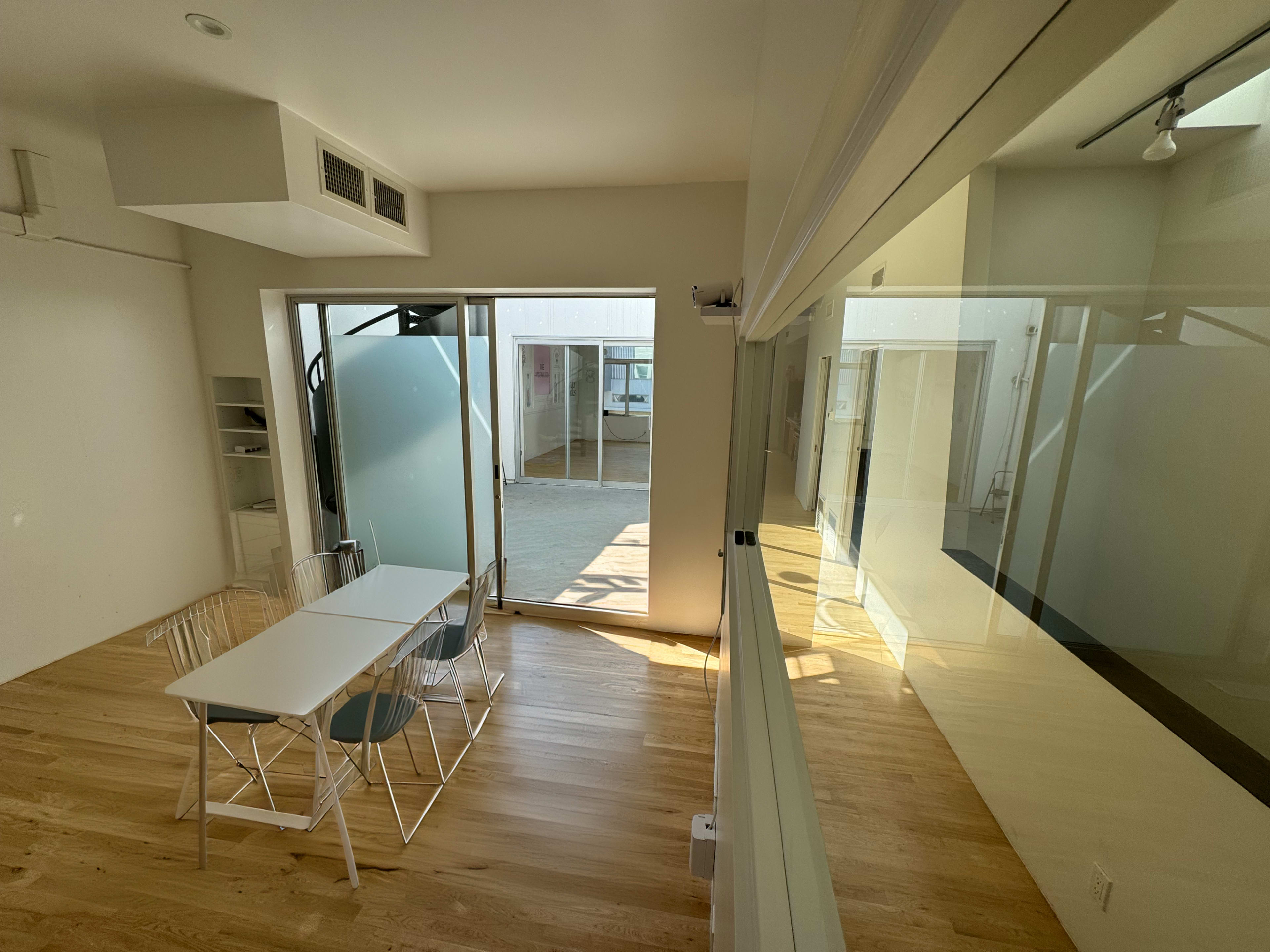 A bright, minimalist office space with a table set for four and large windows that open to an outdoor area.