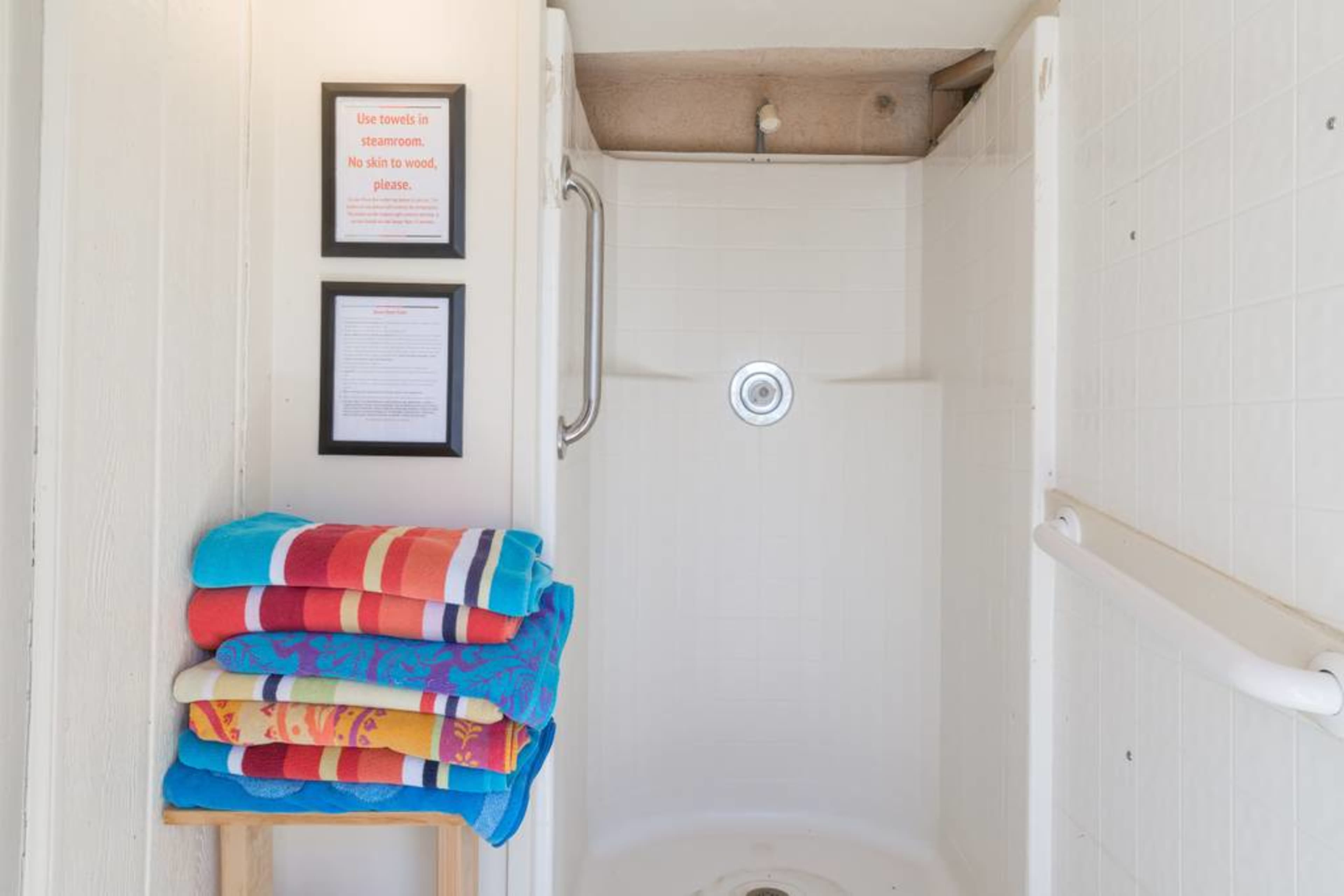 A shower stall with a wooden shelf holding neatly stacked towels and framed signs on the wall.