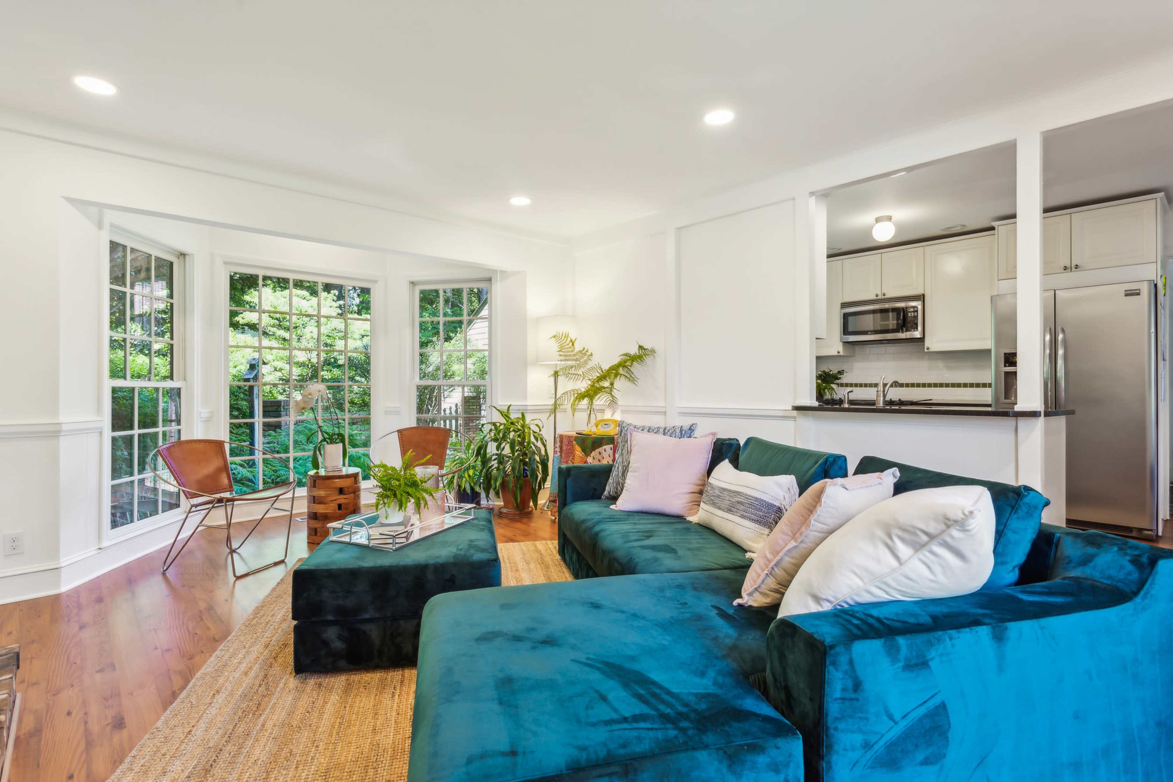 The living room features a blue sectional sofa, a wooden coffee table, and large windows that allow natural light to fill the space.