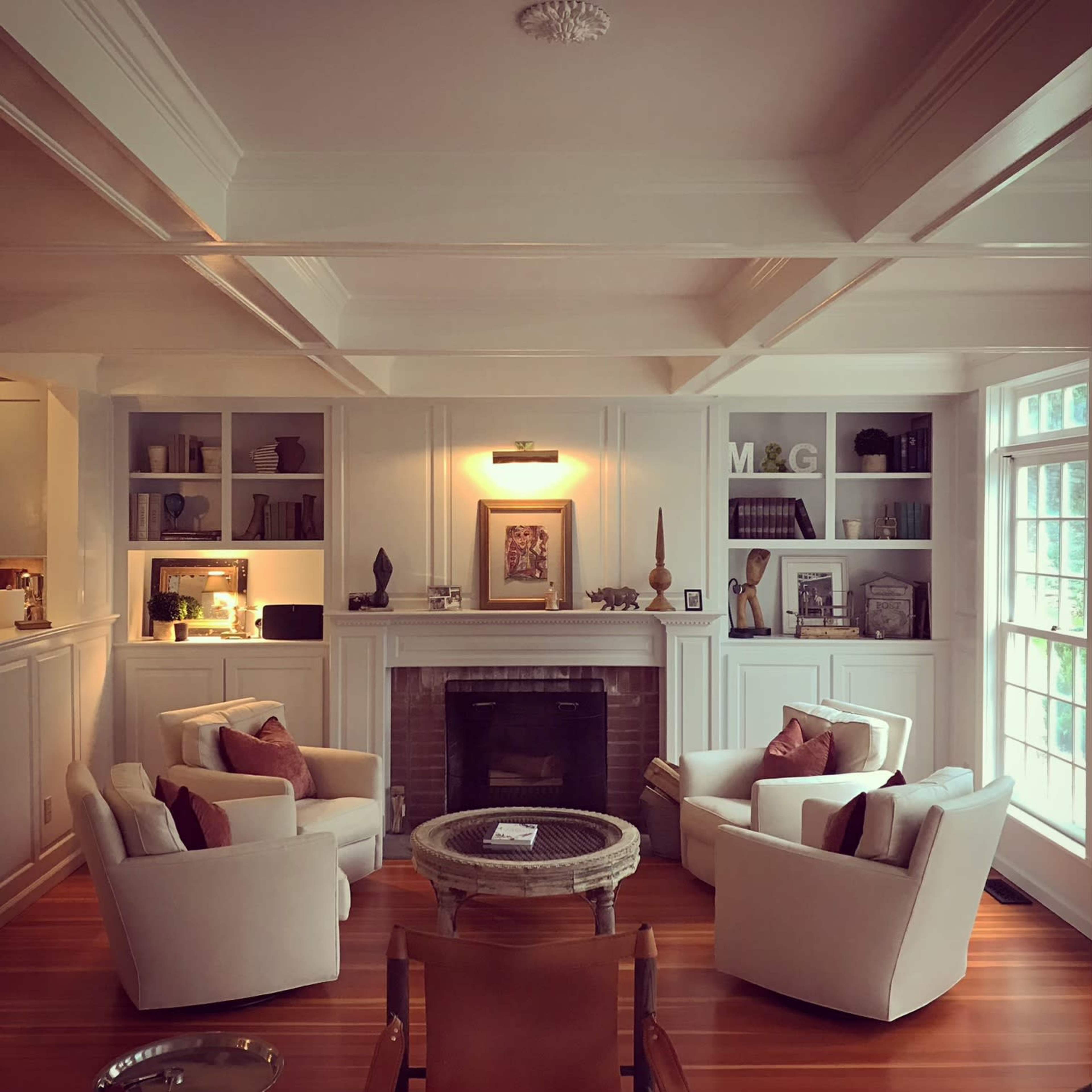 A cozy living room with two white armchairs facing a central fireplace, flanked by built-in shelves filled with books and decorative items.