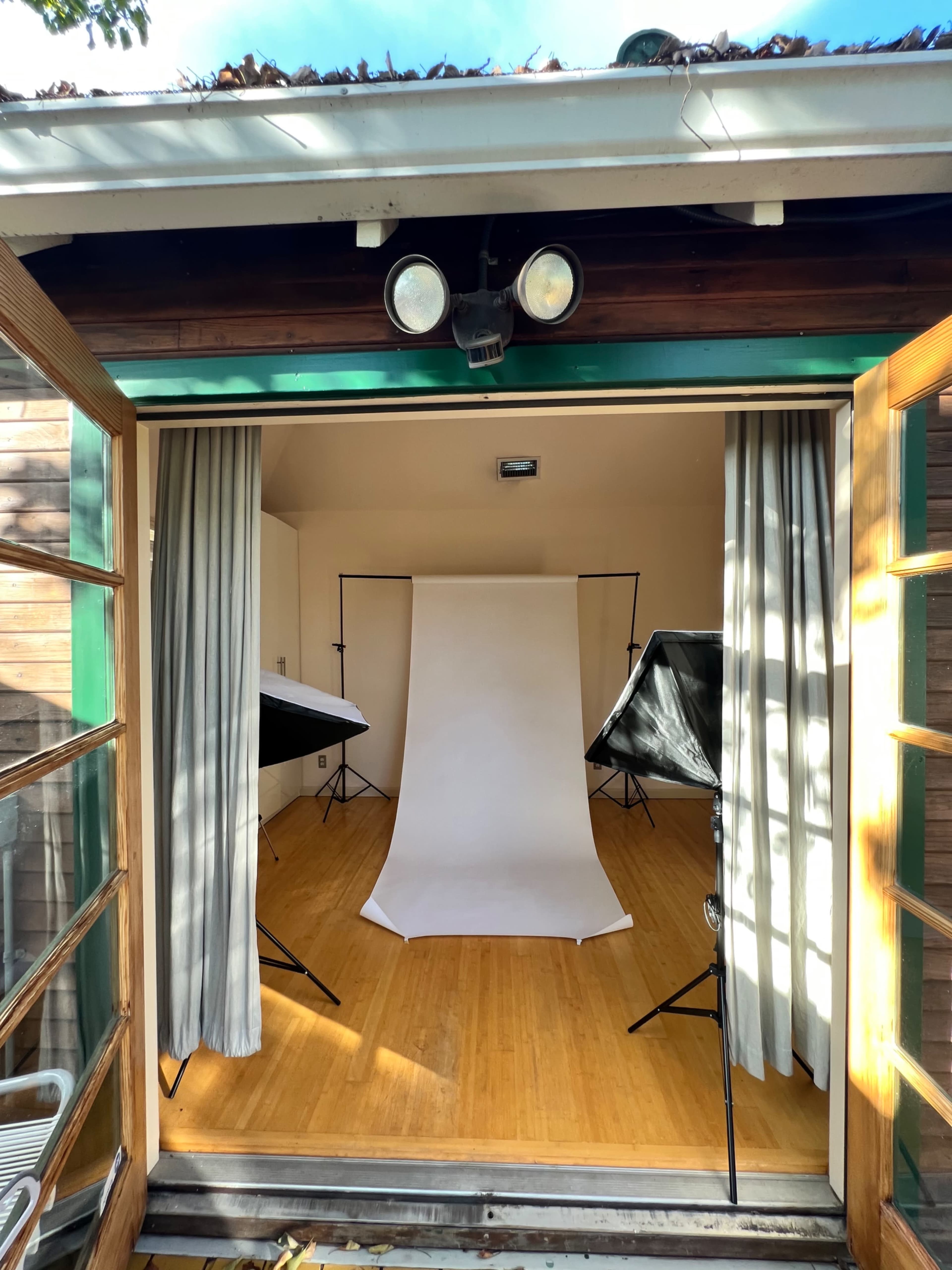 A photo studio with a plain backdrop and multiple softbox lights set up, visible through open double doors.