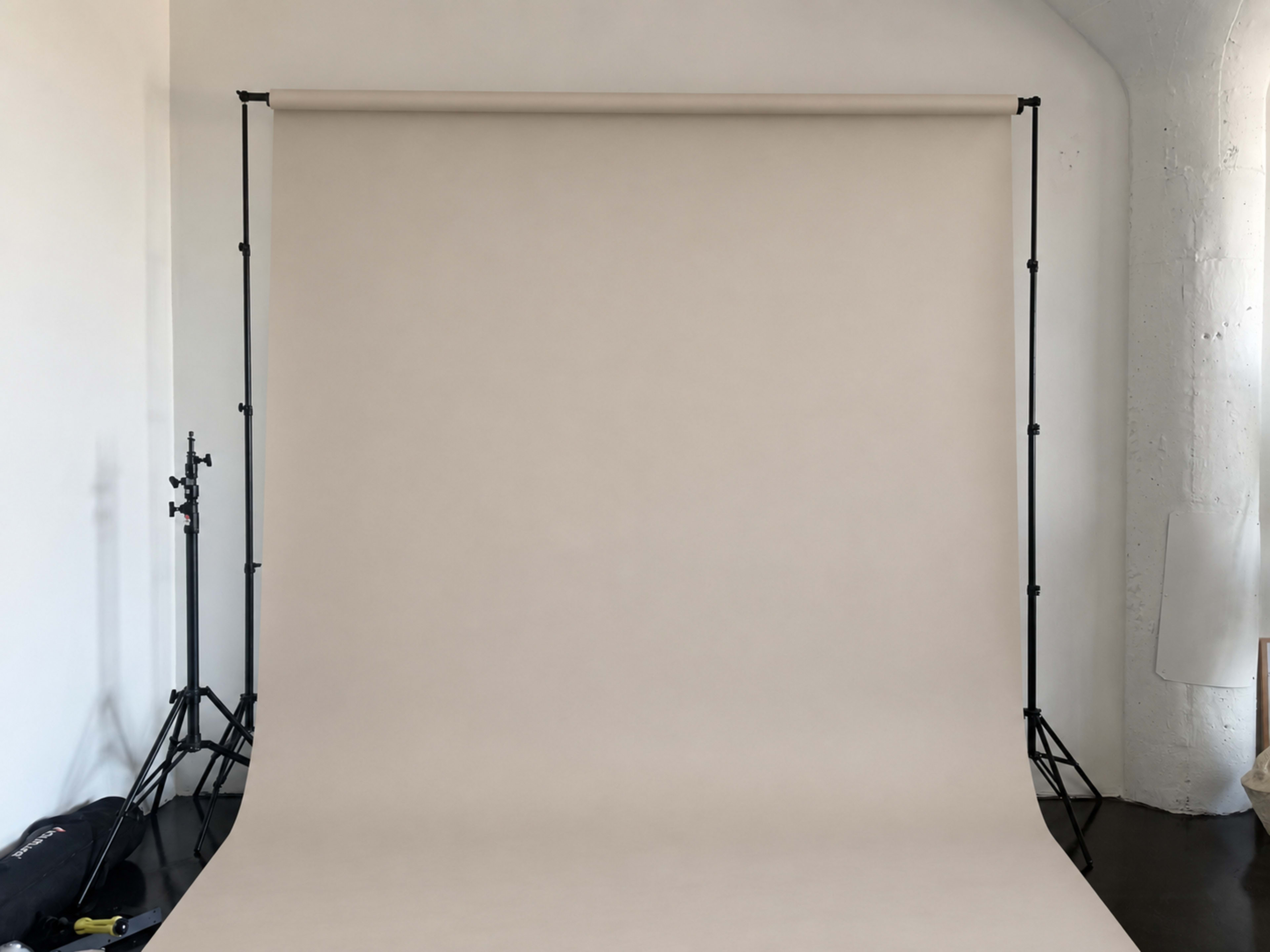 The image shows a photography studio with a plain beige backdrop supported by black stands.