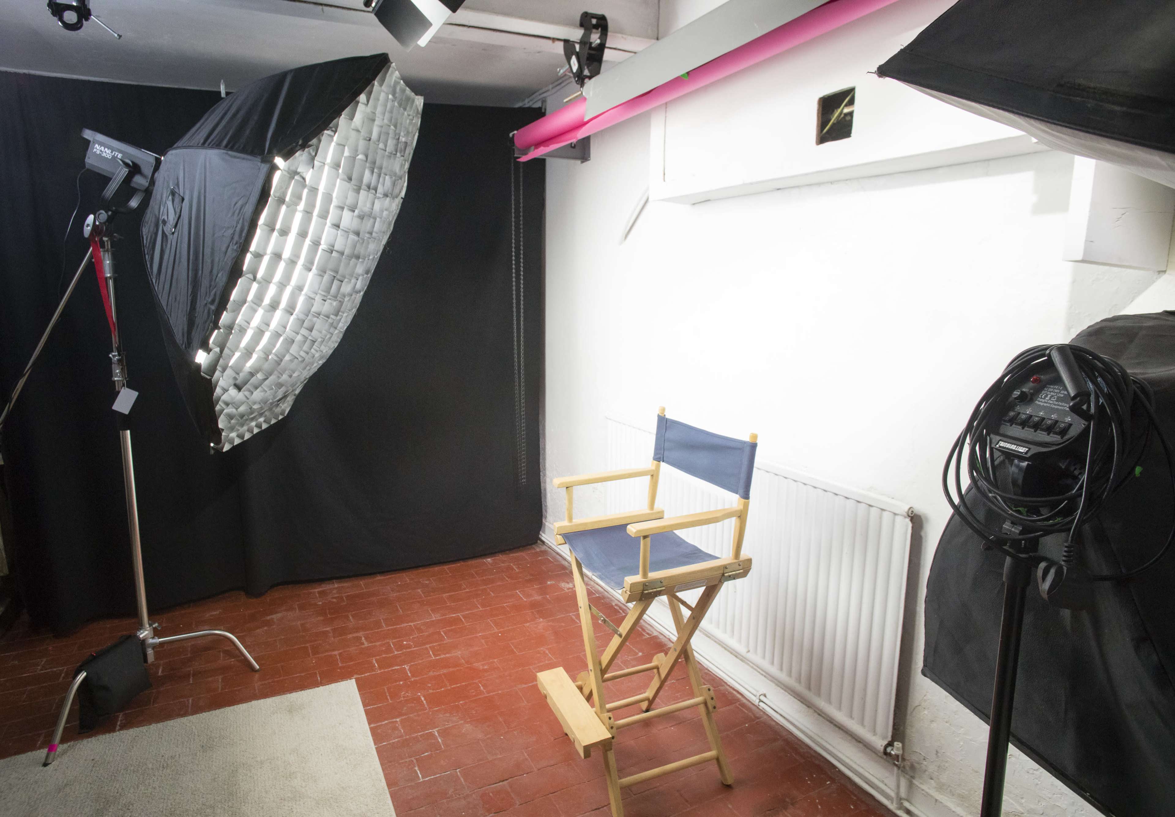 A well-lit photography studio featuring a director's chair, softbox lighting, and a black backdrop.