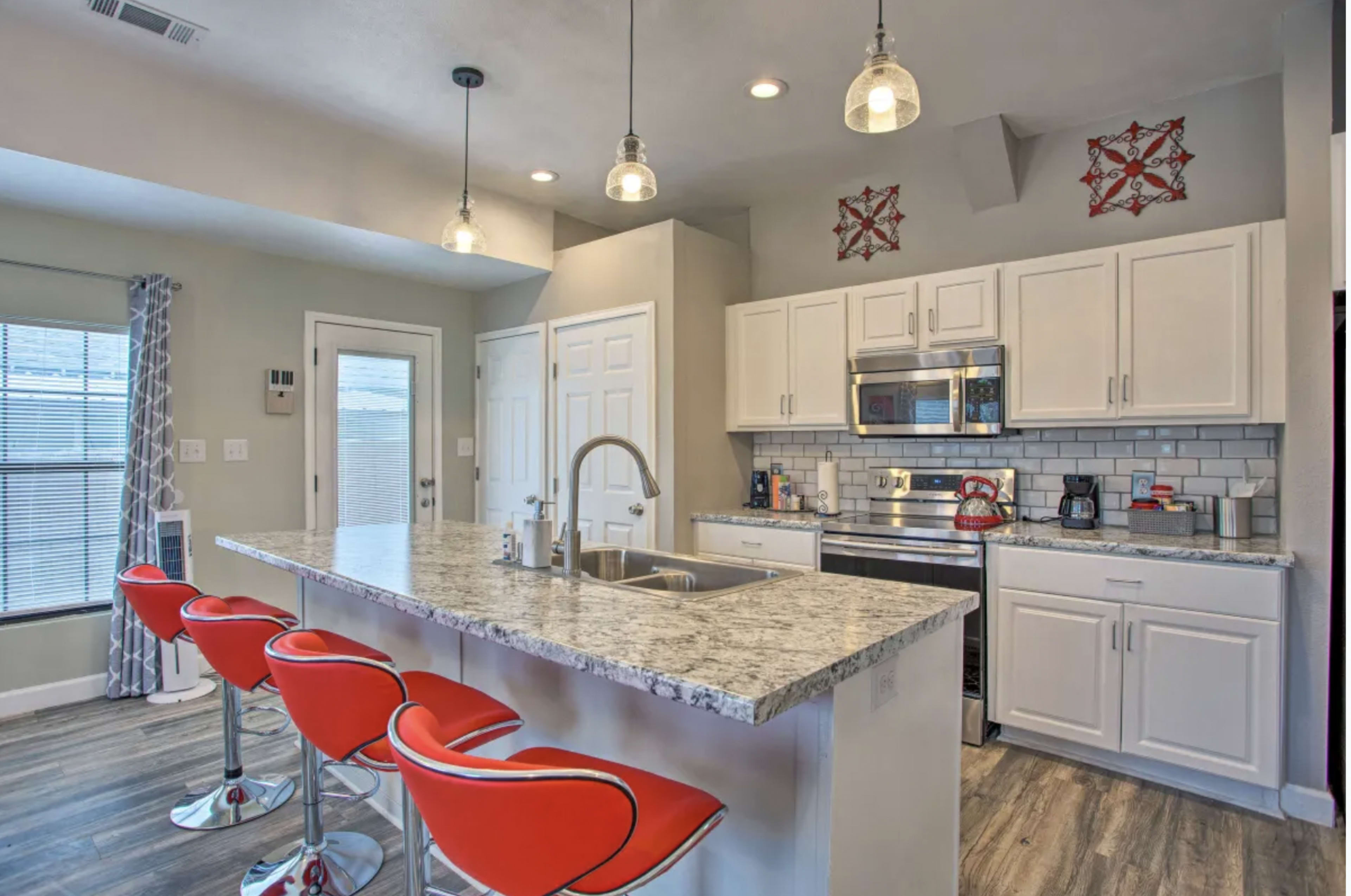 A modern kitchen features a central island with red bar stools, stainless steel appliances, and white cabinetry.