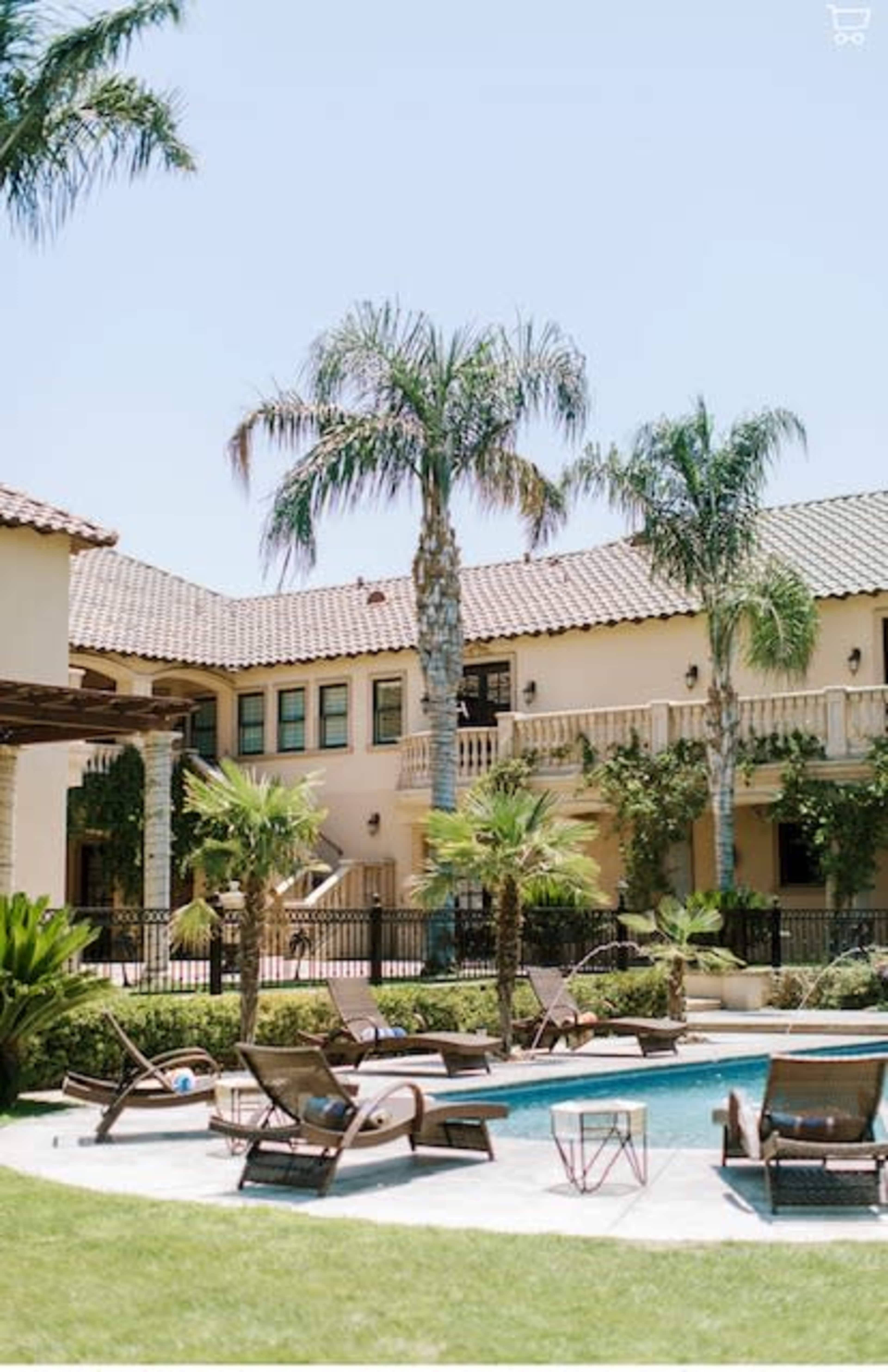 A pool area is surrounded by lounge chairs and palm trees in front of a two-story building.