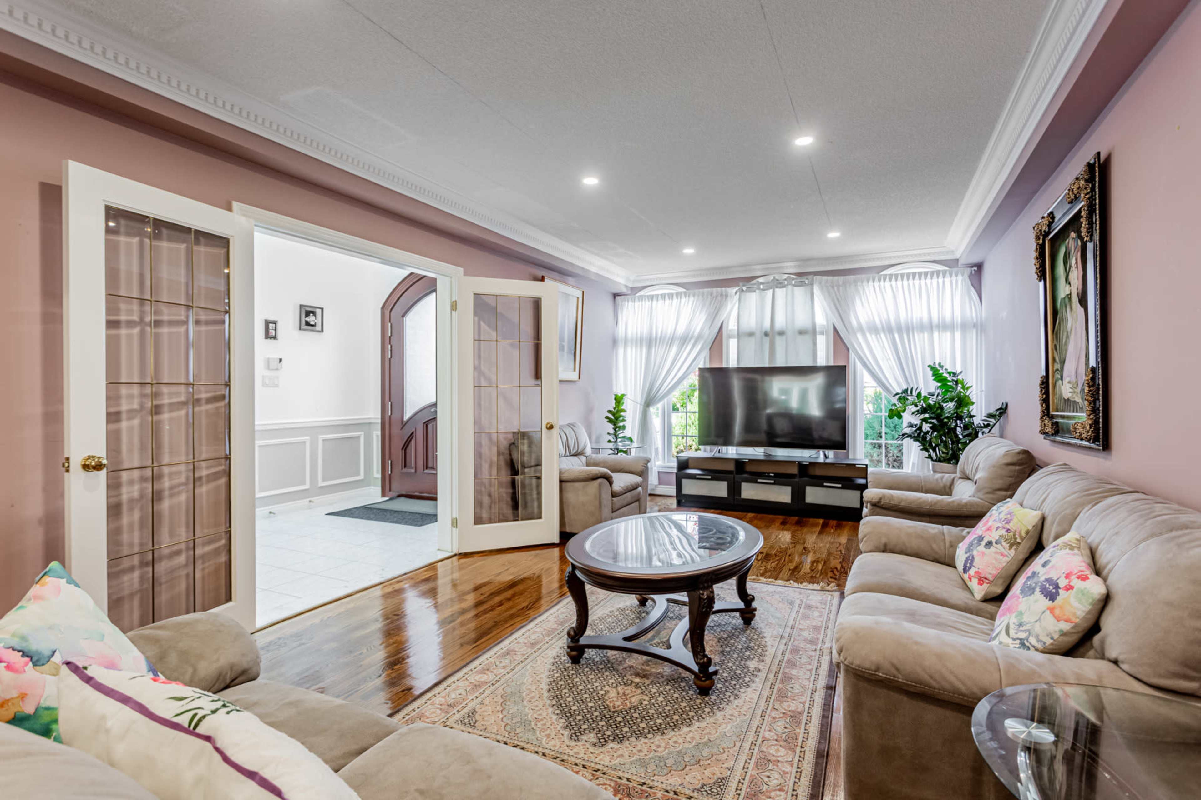 A living room with beige sofas, a round coffee table, and large windows dressed with sheer curtains.