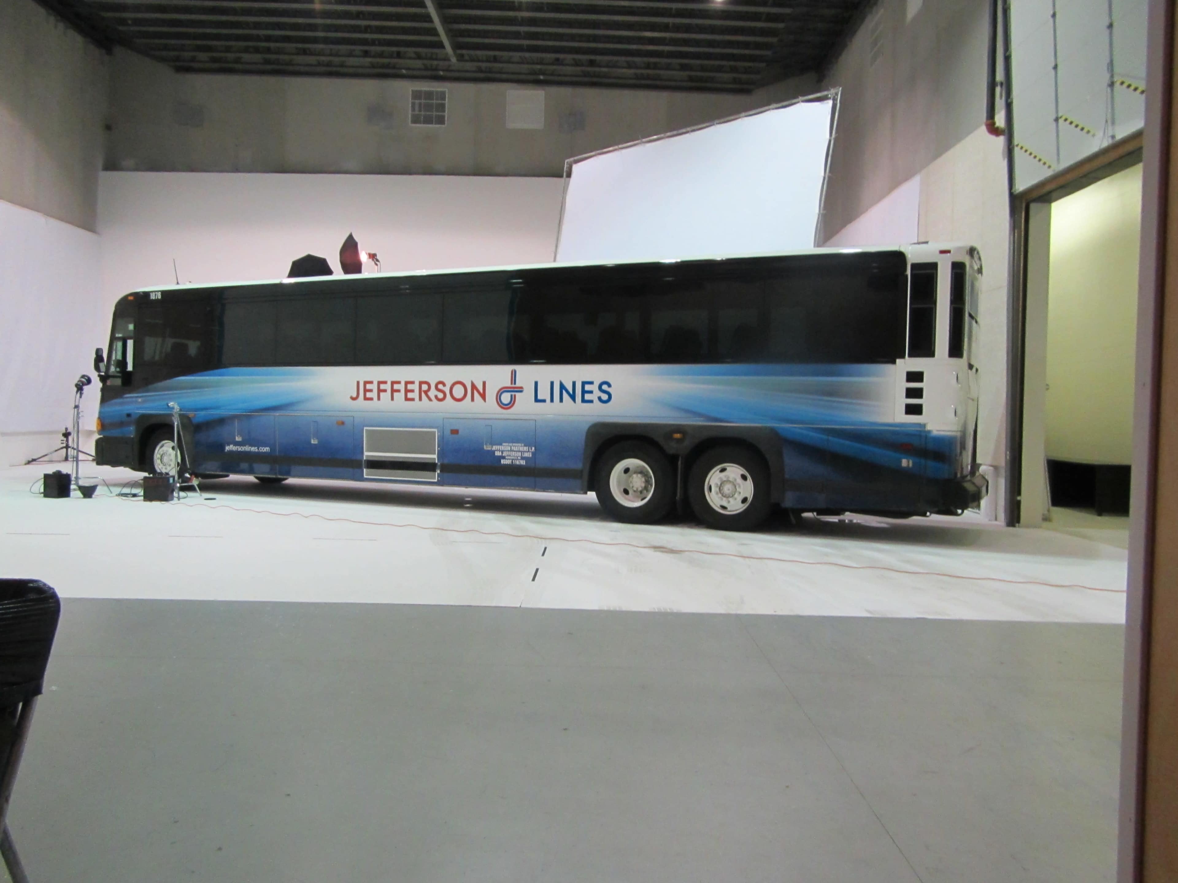 A Jefferson Lines bus is parked on a white backdrop inside a studio.
