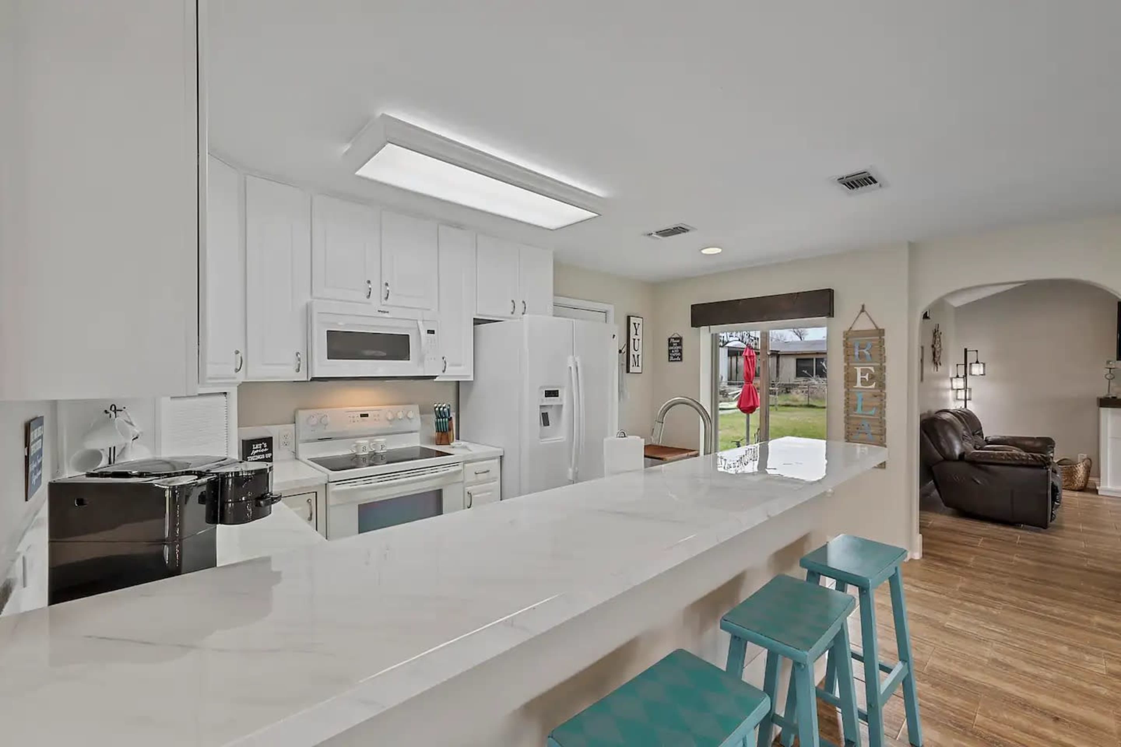 A modern kitchen features white cabinetry, a large island with teal stools, and appliances including a microwave and refrigerator.