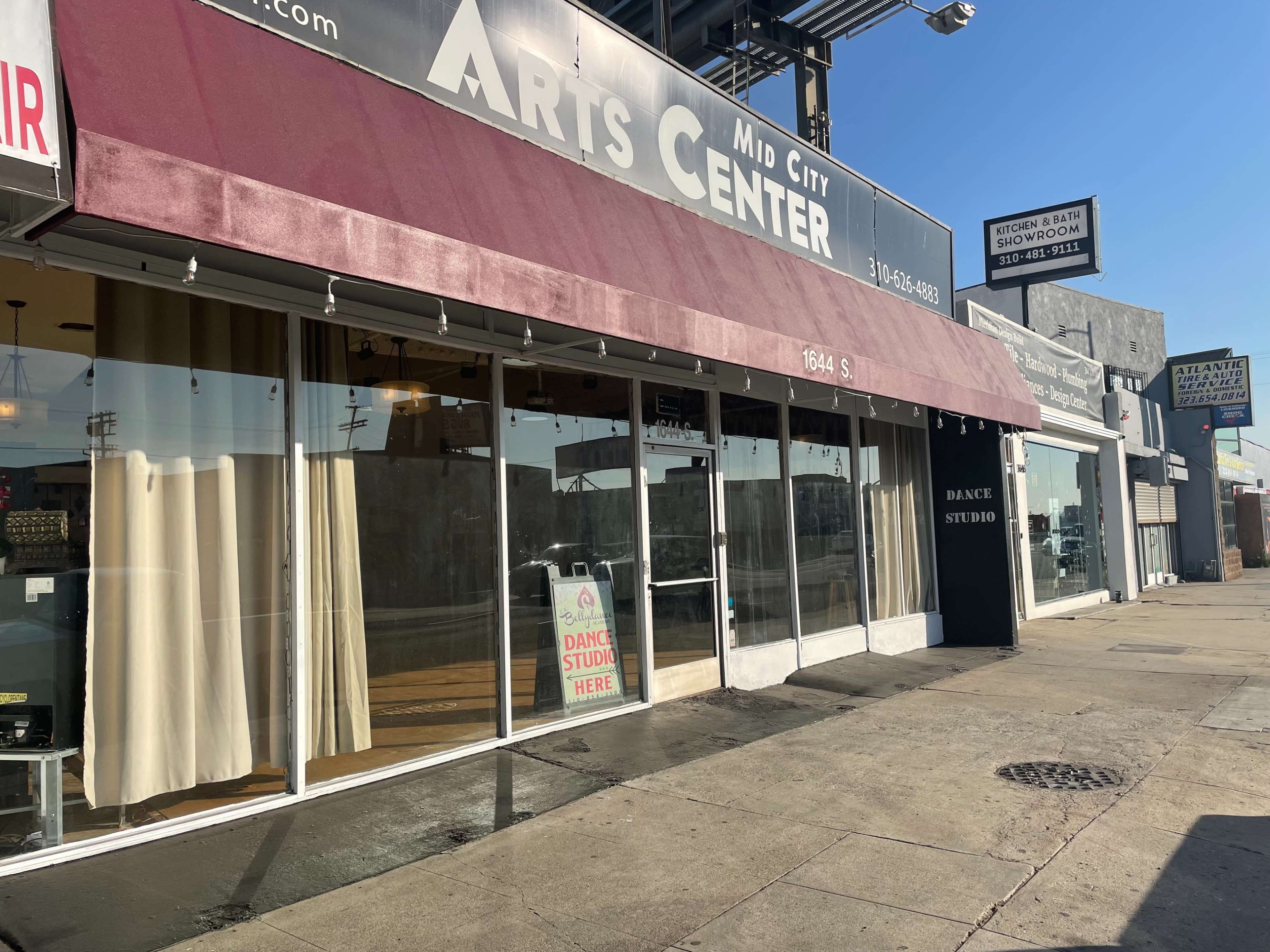 The image shows the exterior of the Mid City Arts Center, featuring large windows and a maroon awning, with a sign indicating a dance studio inside.