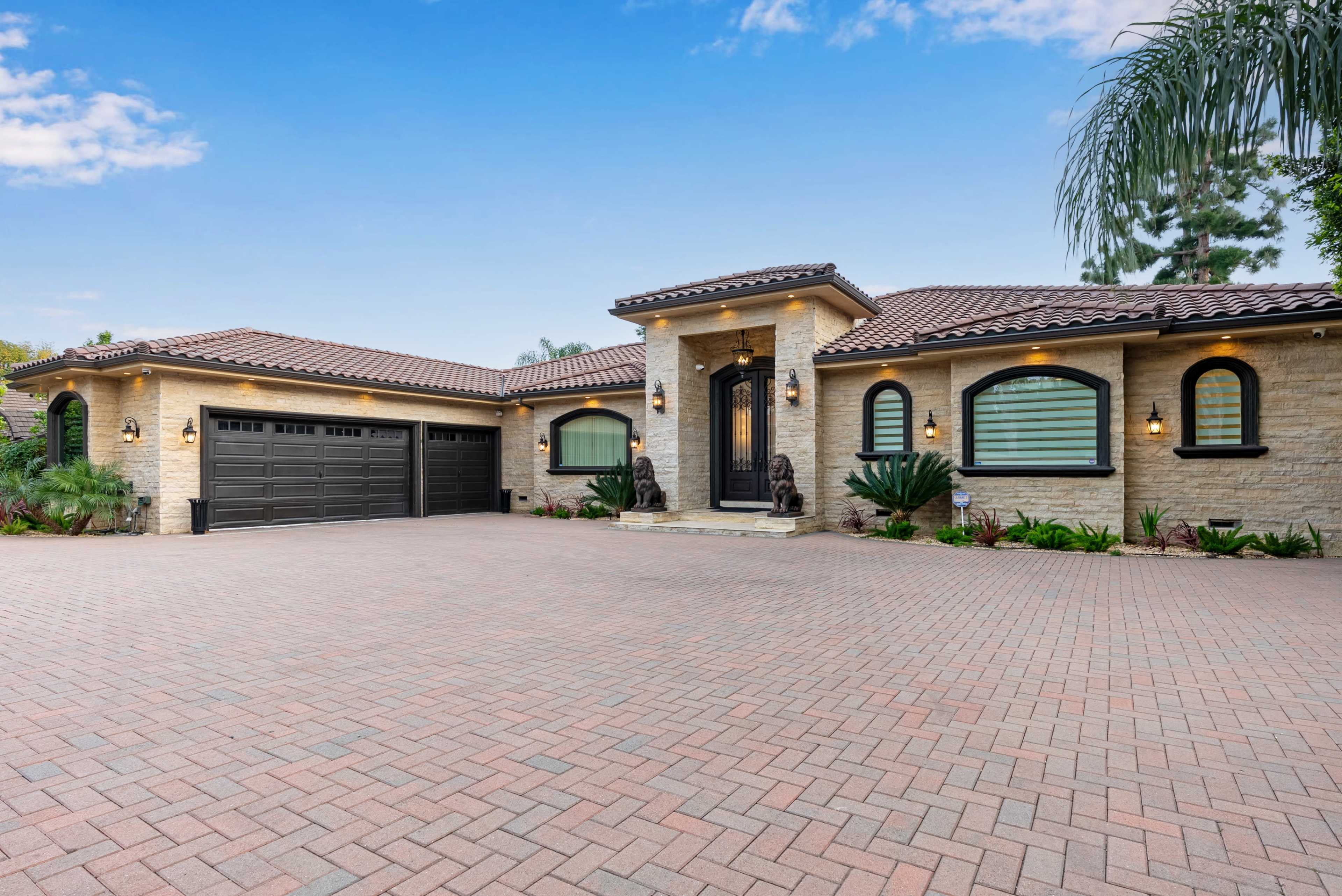 The image shows a single-story luxury home with a brick driveway, a tiled roof, and decorative landscaping.