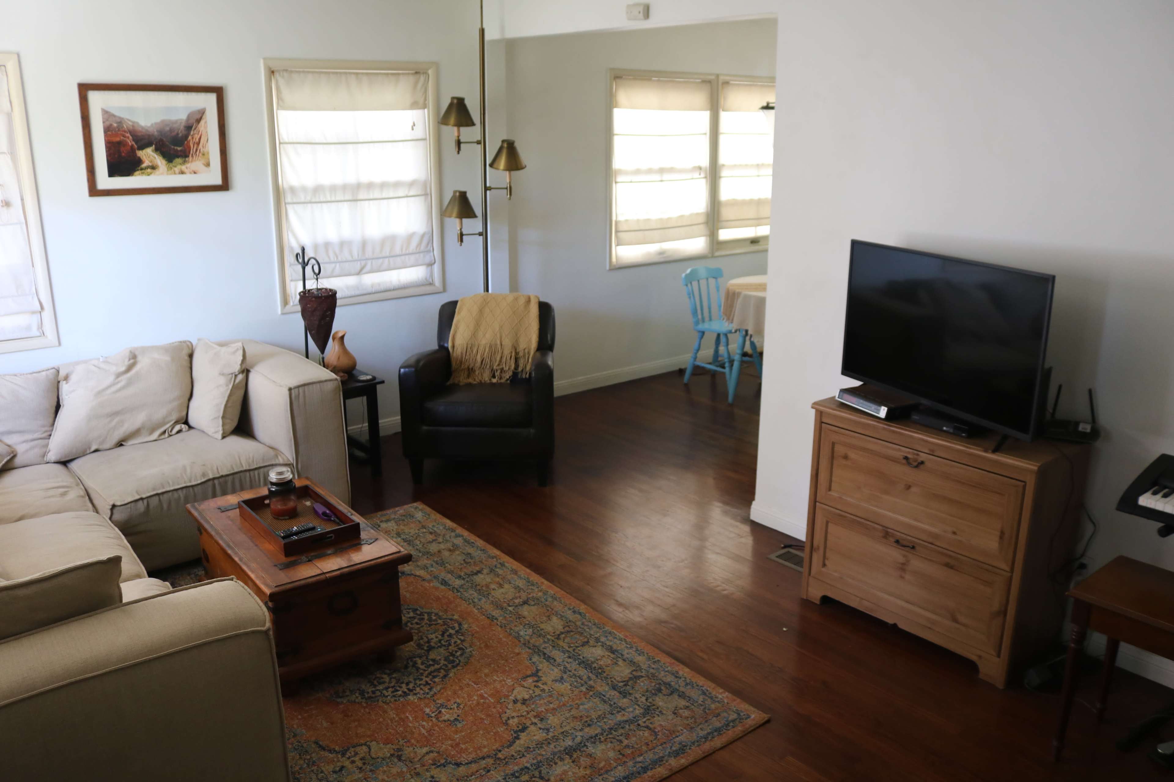 A living room with a beige sofa, a wooden coffee table, a television on a cabinet, and a chair beside a small dining area.