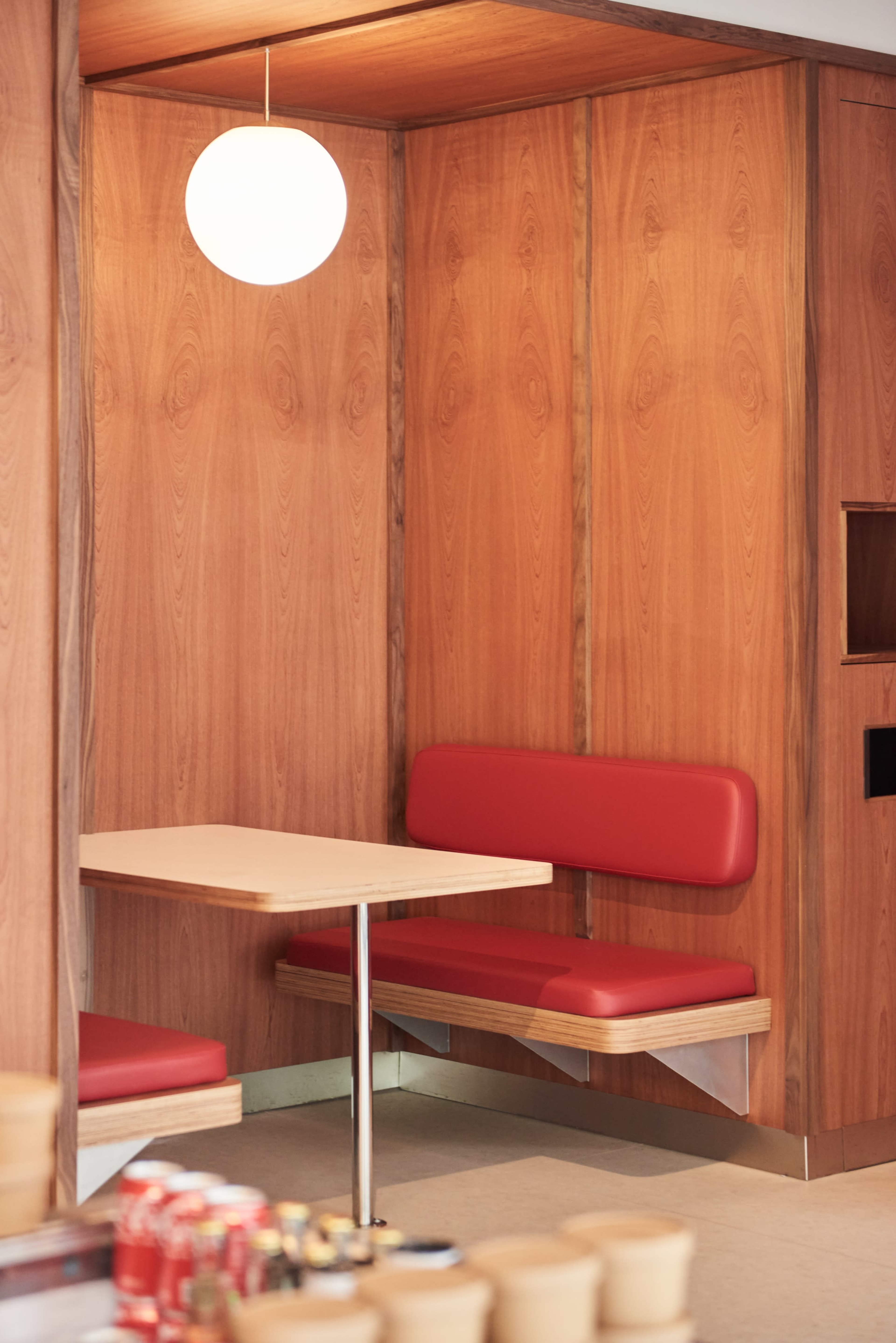 A cozy seating area features a wooden booth with a red bench and a small table under a round light fixture.