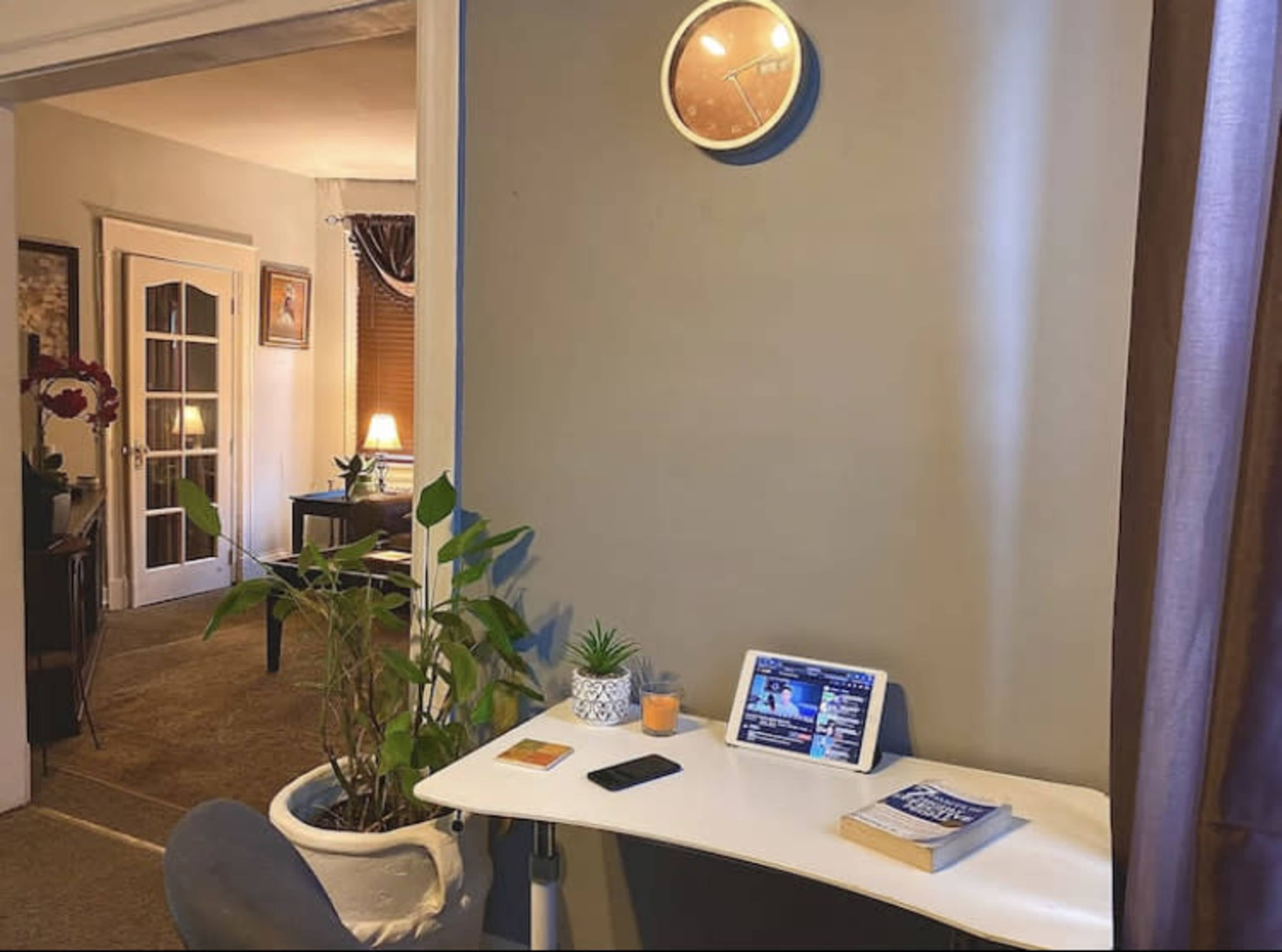A small table with a tablet, a phone, and houseplants is positioned against a wall in a room that has a doorway leading to another area.