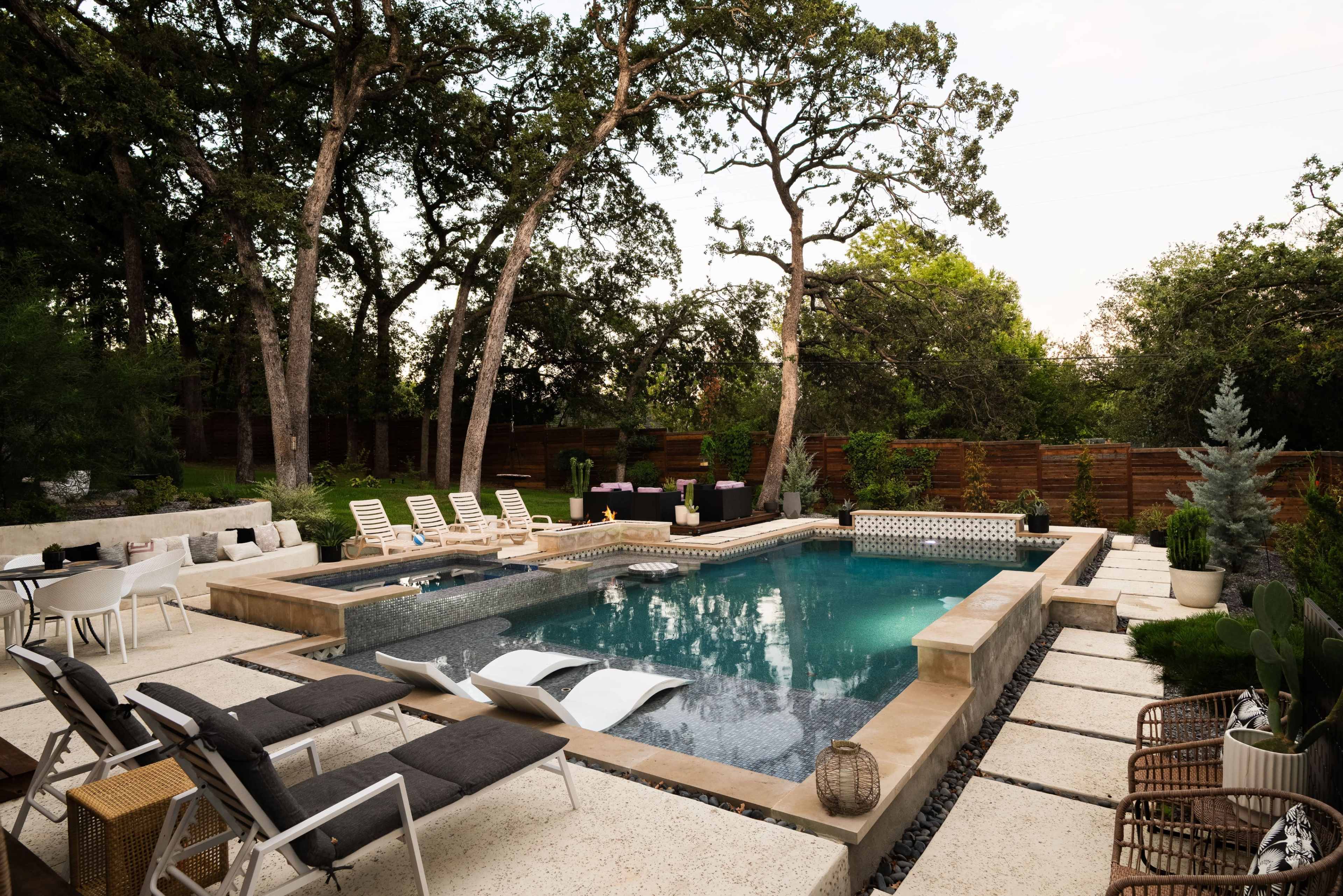 The image shows a modern backyard with a rectangular swimming pool, surrounded by lounge chairs, decorative plants, and a wooden fence.