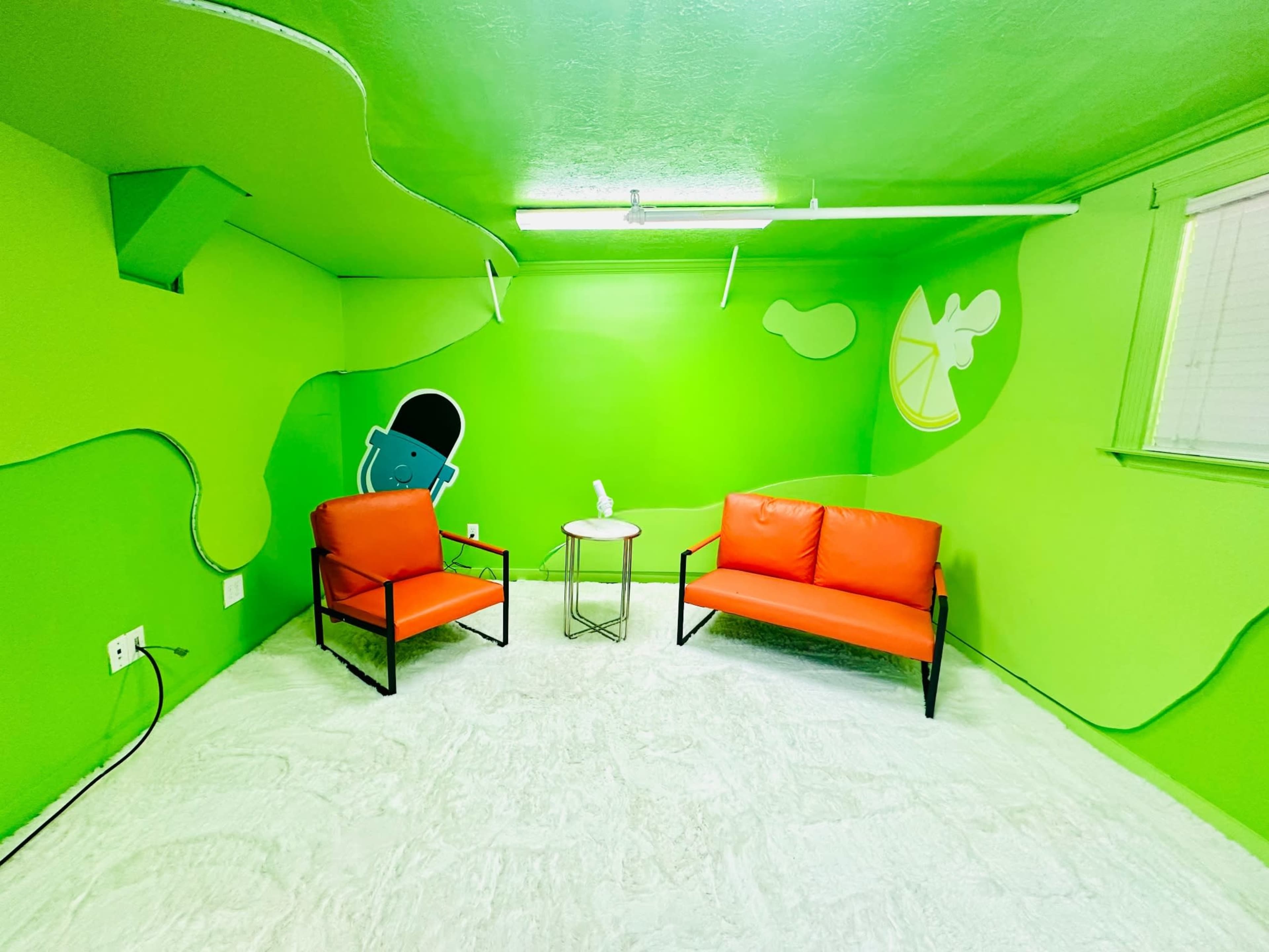 The image shows a brightly colored green room with two orange sofas and a small table, featuring a cartoonish figure on the wall.