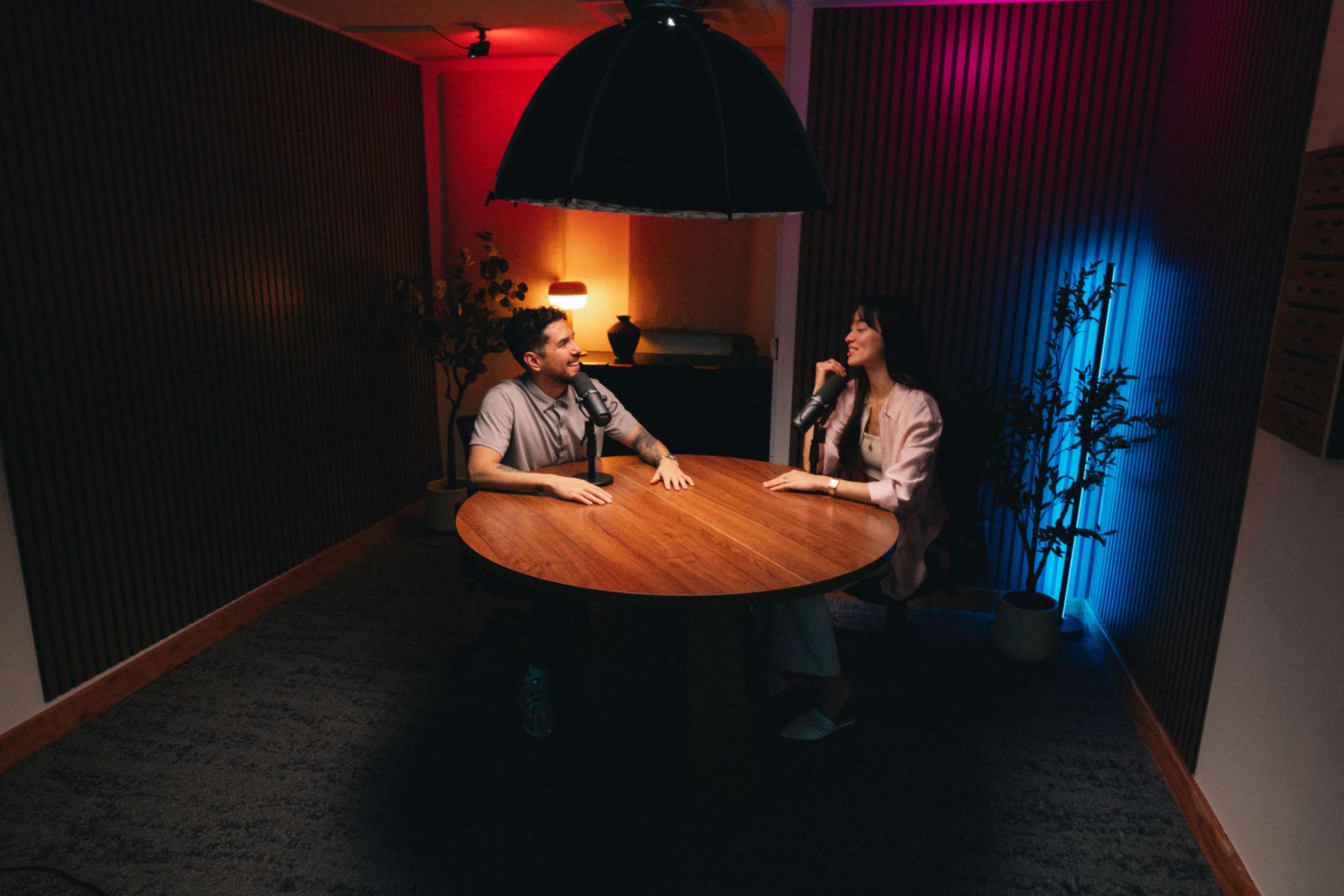 Two individuals are seated at a round wooden table in a well-lit room with colorful ambient lighting.