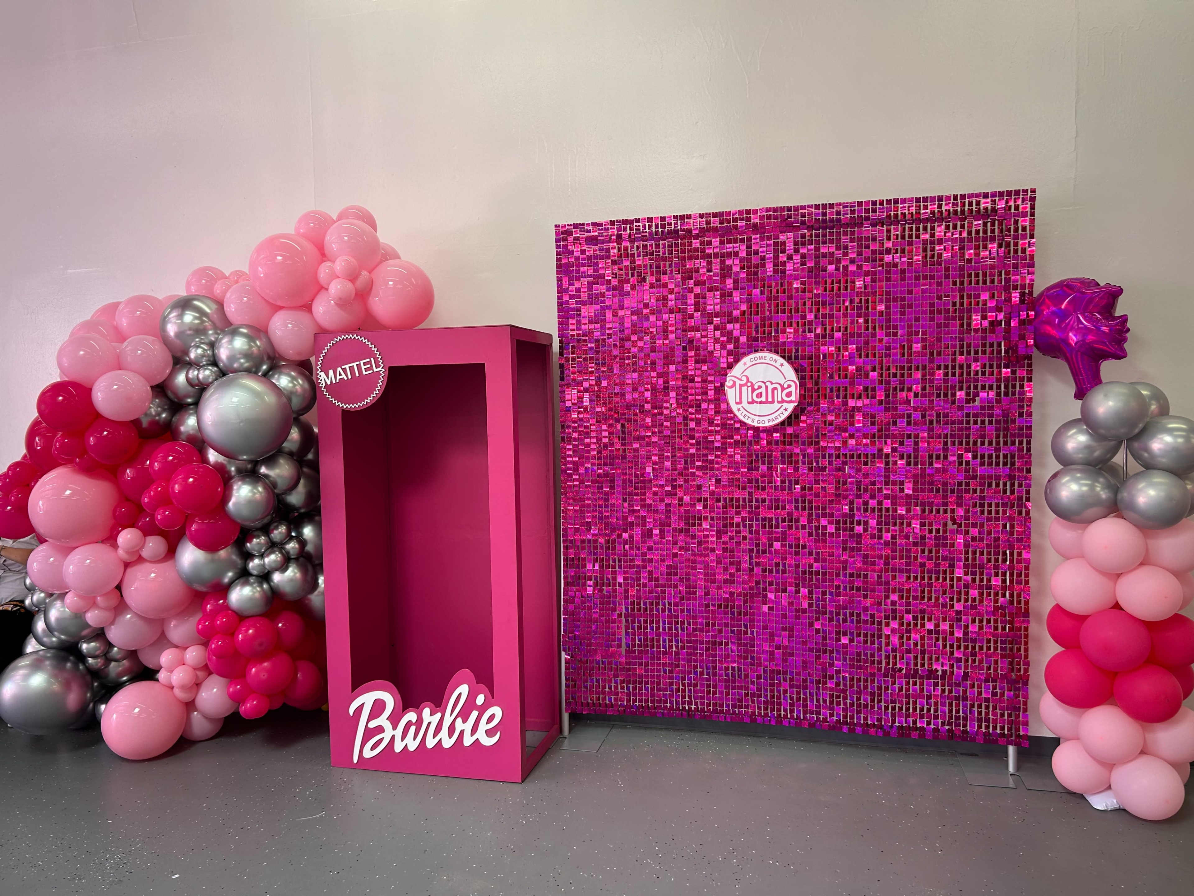 A vibrant party setup with a pink balloon arch on the left and a sparkling pink backdrop adorned with a circular logo on the right.