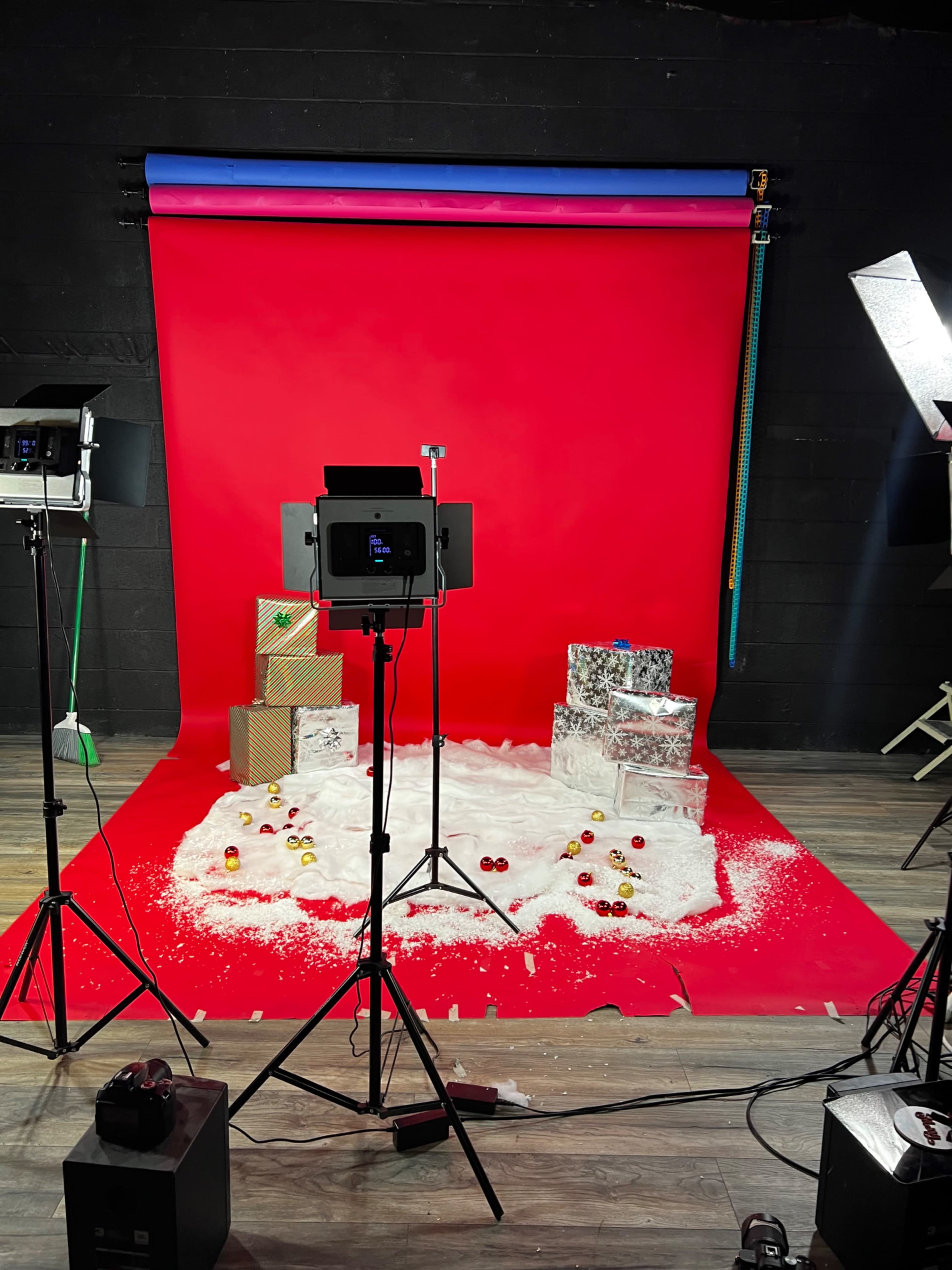 A photography studio set up with red backdrops, decorated gift boxes, and artificial snow on the floor.