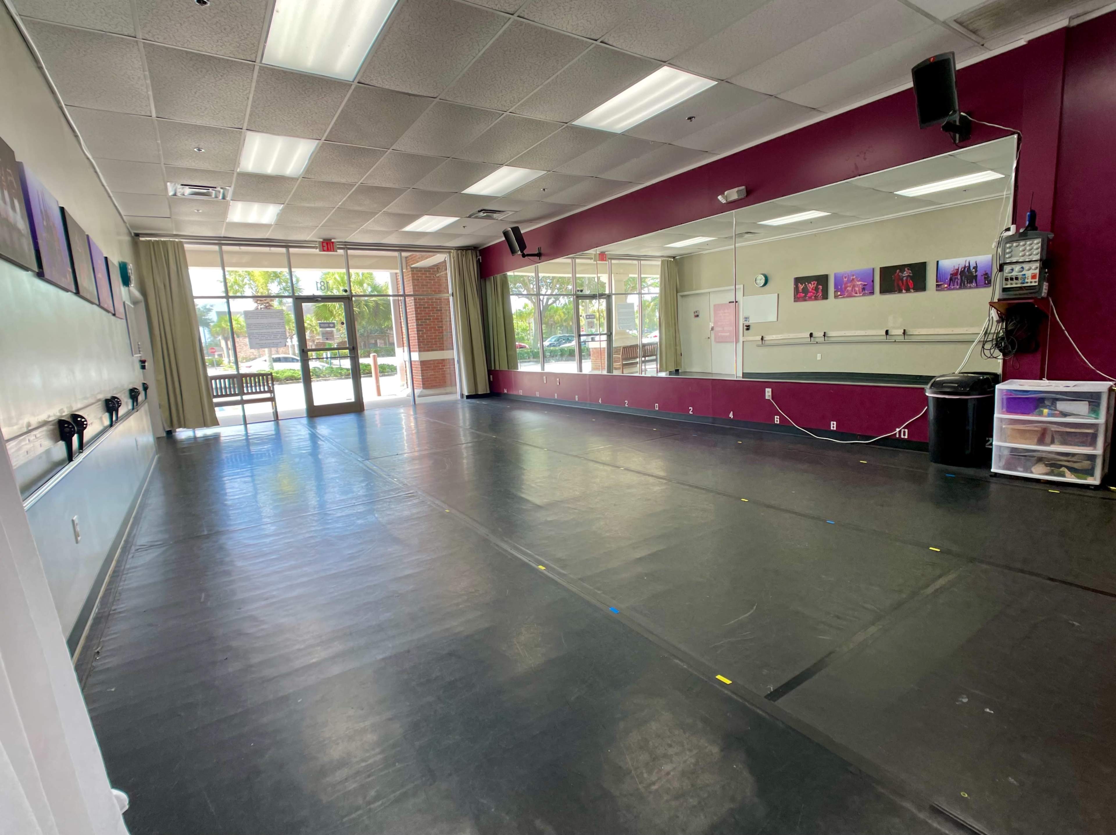 A spacious dance studio with a mirrored wall and large windows allowing natural light to enter.