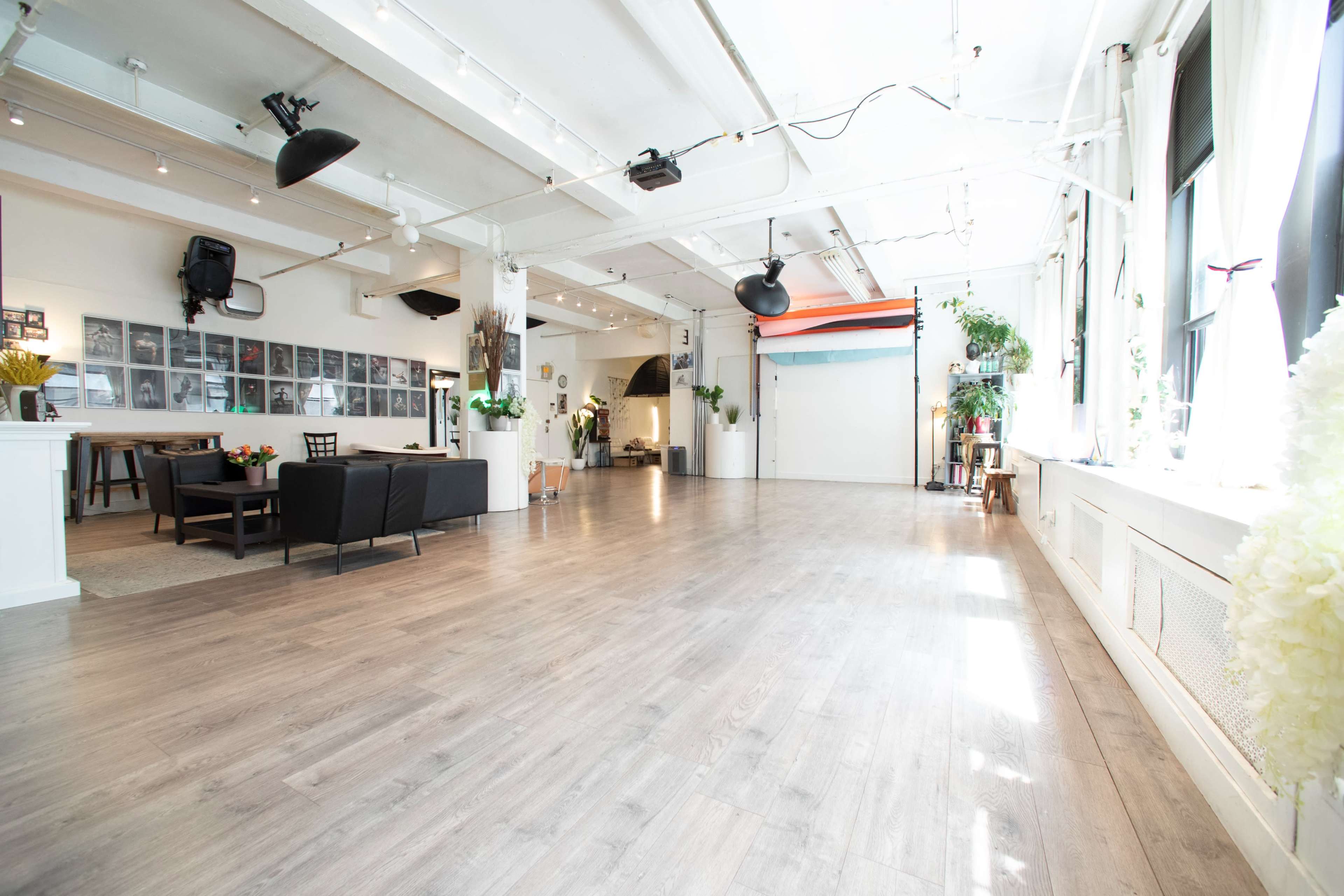 The image shows a large, open interior space with wooden flooring, bright lighting, and a few seating areas and decorative plants.