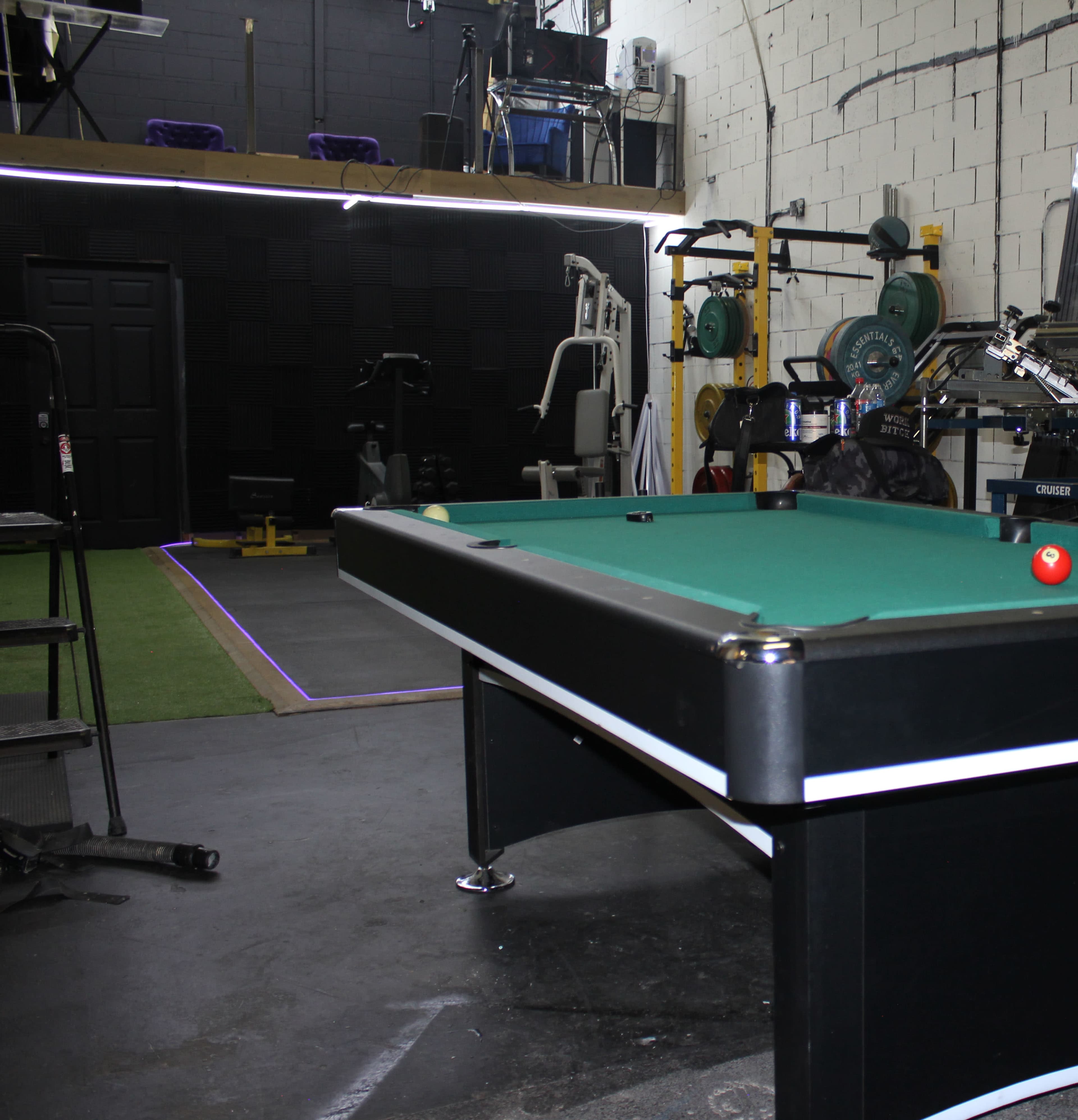 A pool table in the foreground with exercise equipment and gym facilities in the background.
