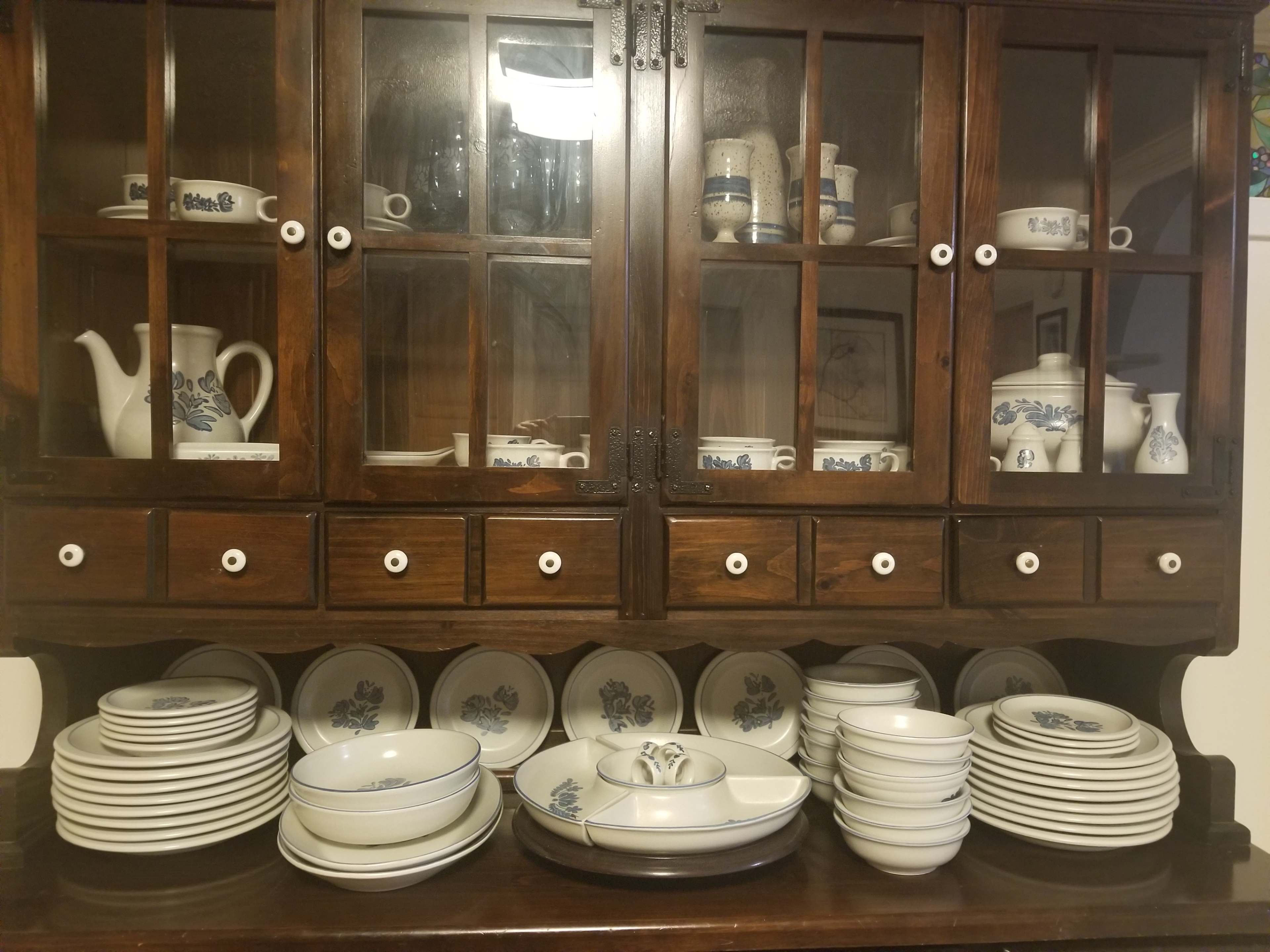 A wooden cabinet displays a collection of blue and white ceramic dinnerware, including plates, bowls, and decorative pieces.