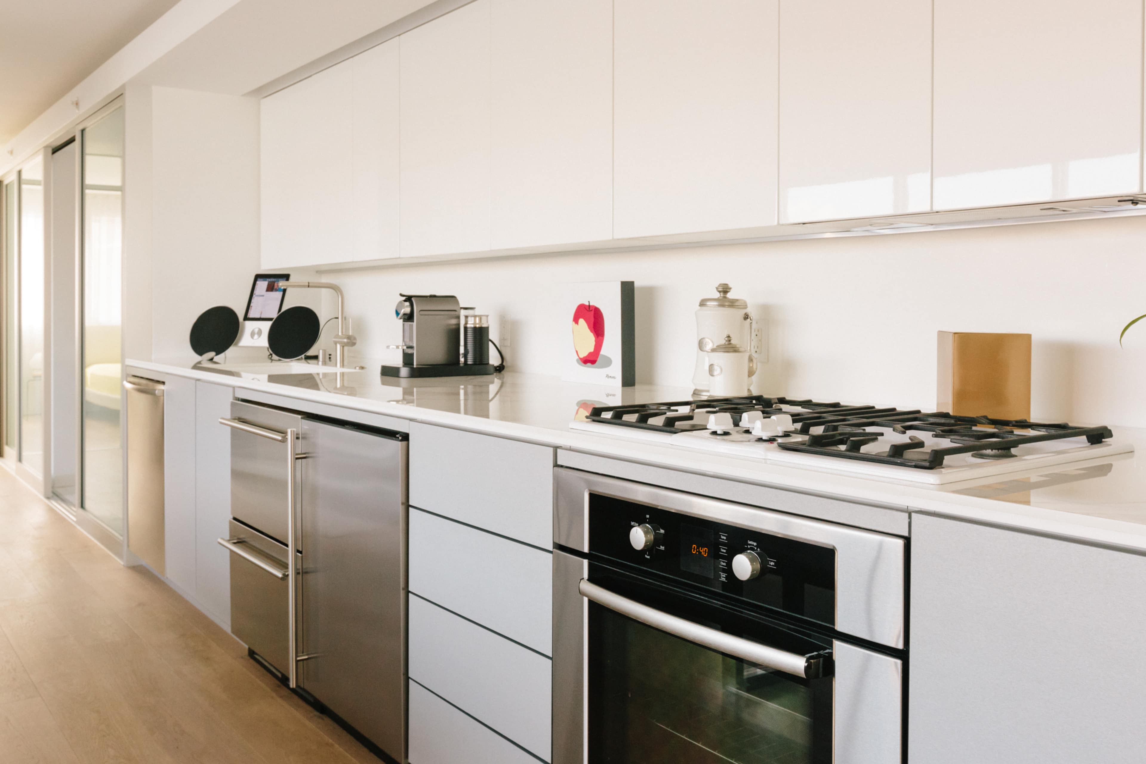 A modern kitchen with sleek white cabinets, a stainless steel fridge, a gas stove, and a minimalistic design.