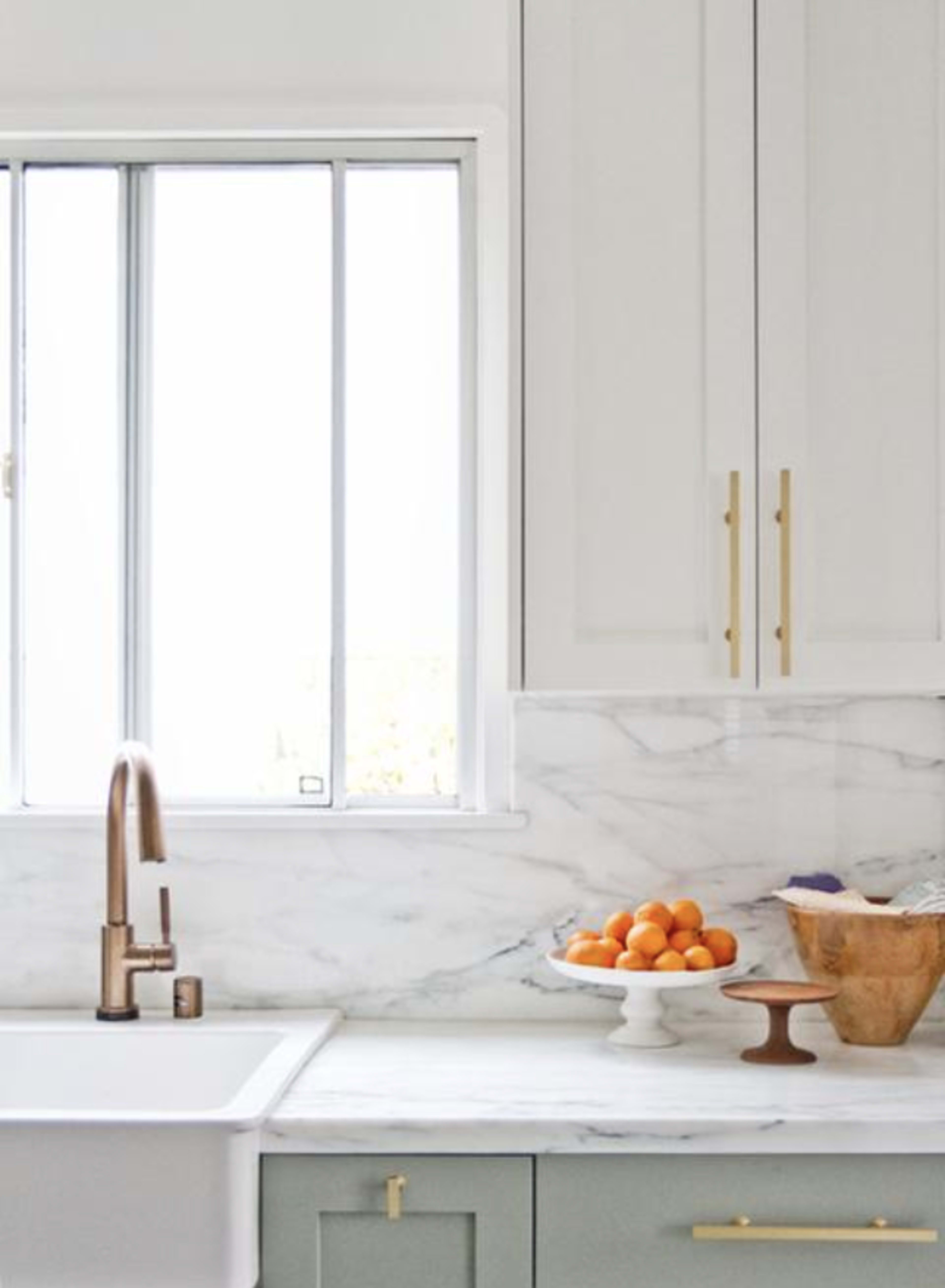 A kitchen scene features a marble countertop with a fruit bowl of oranges, a wooden bowl, and a sleek faucet beside a window.