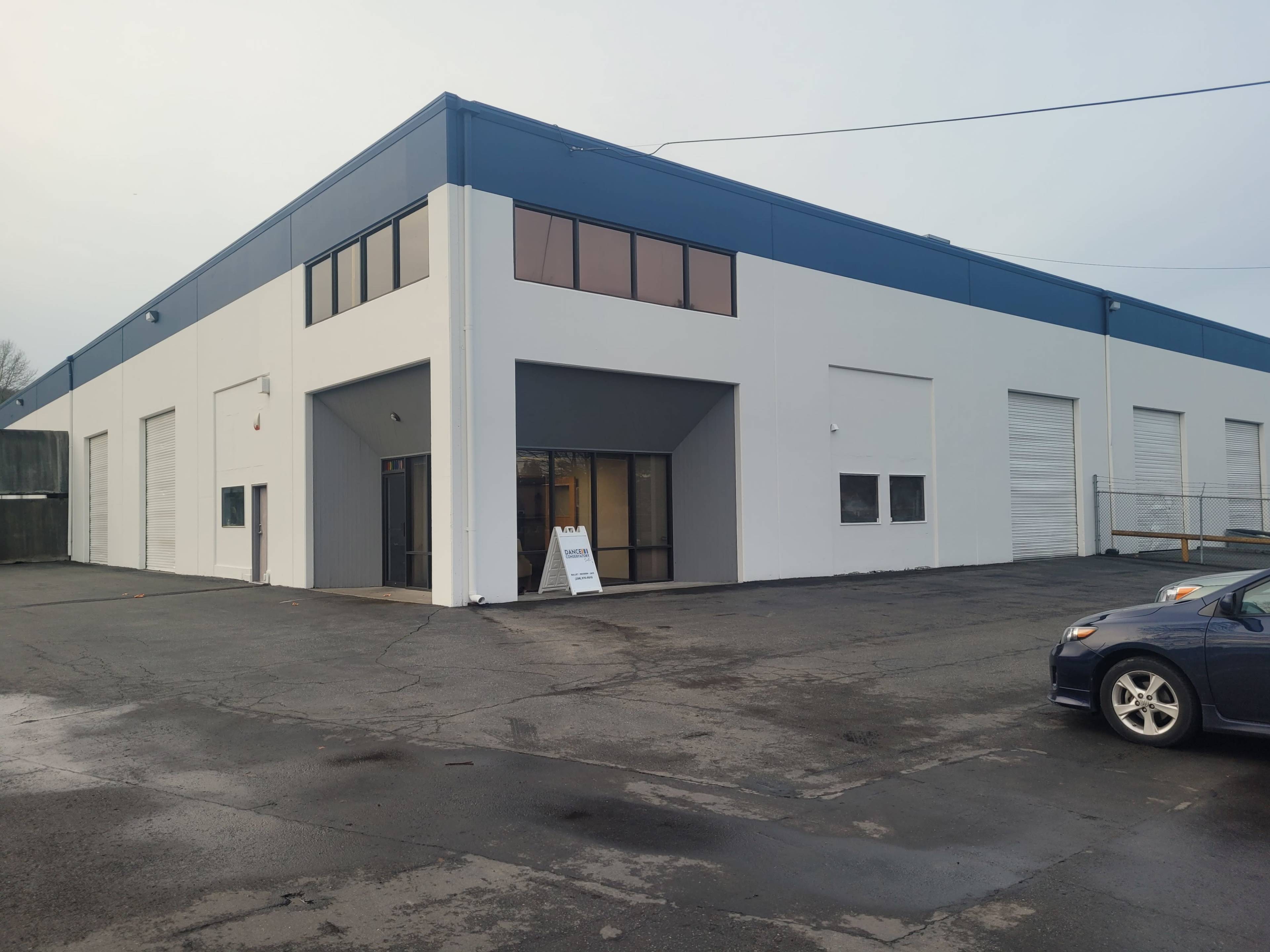 A large, industrial building with a blue and white exterior, featuring multiple garage doors and a sign in front.