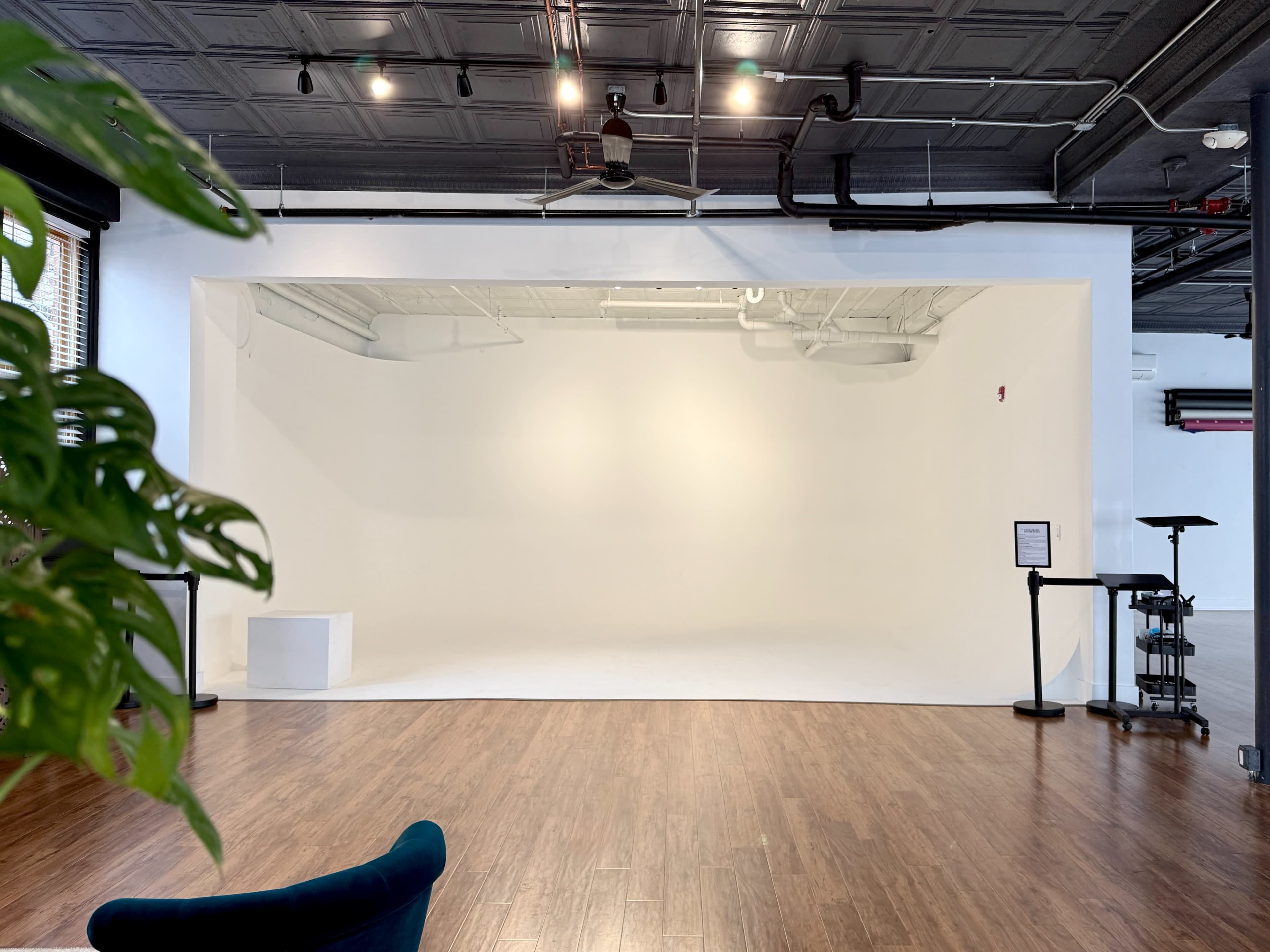 The image shows a spacious, empty studio with a white backdrop, hardwood flooring, and minimal furnishings.