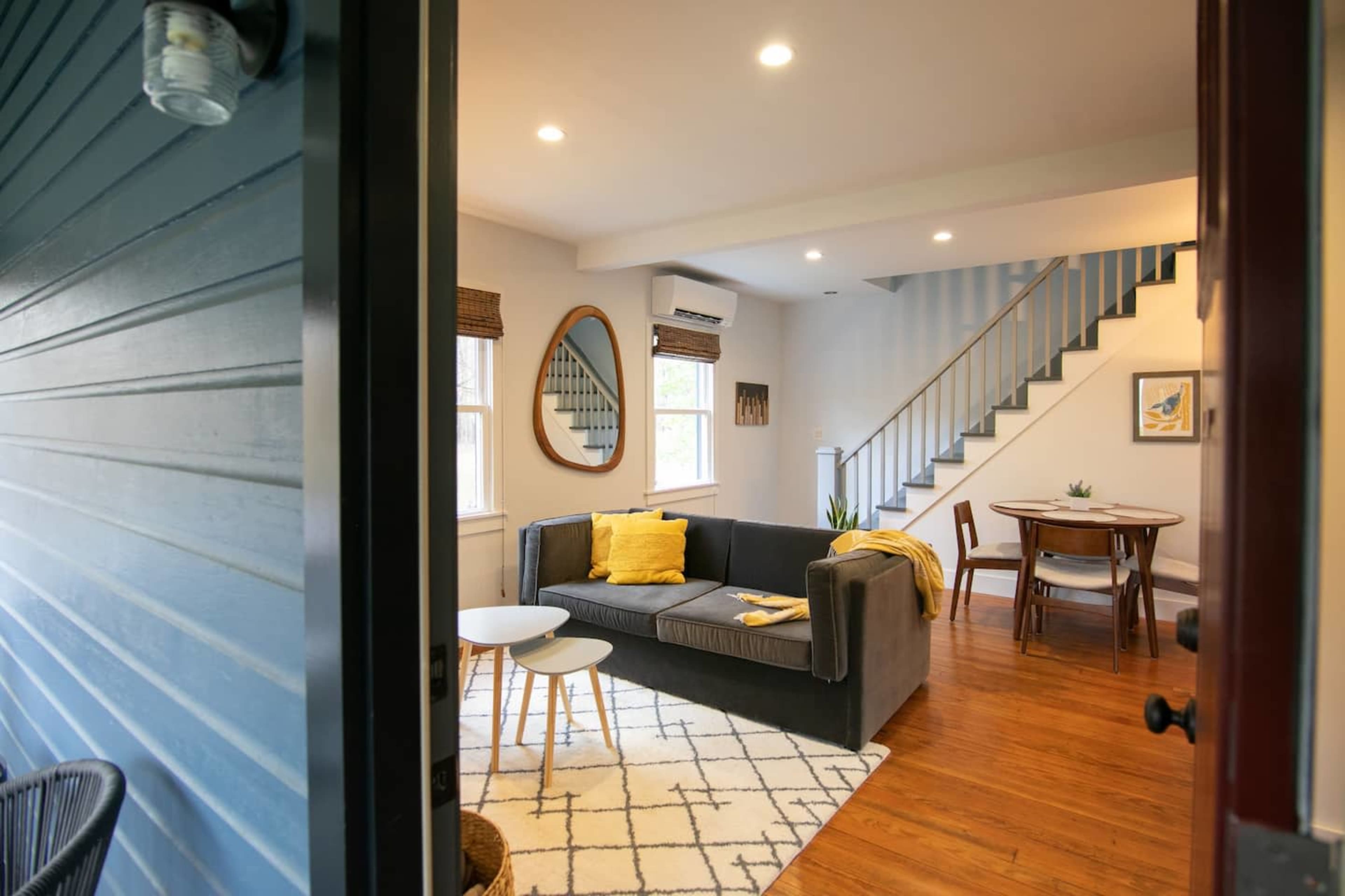 A modern living space with a gray sofa, a dining table, and a staircase leading to an upper level.