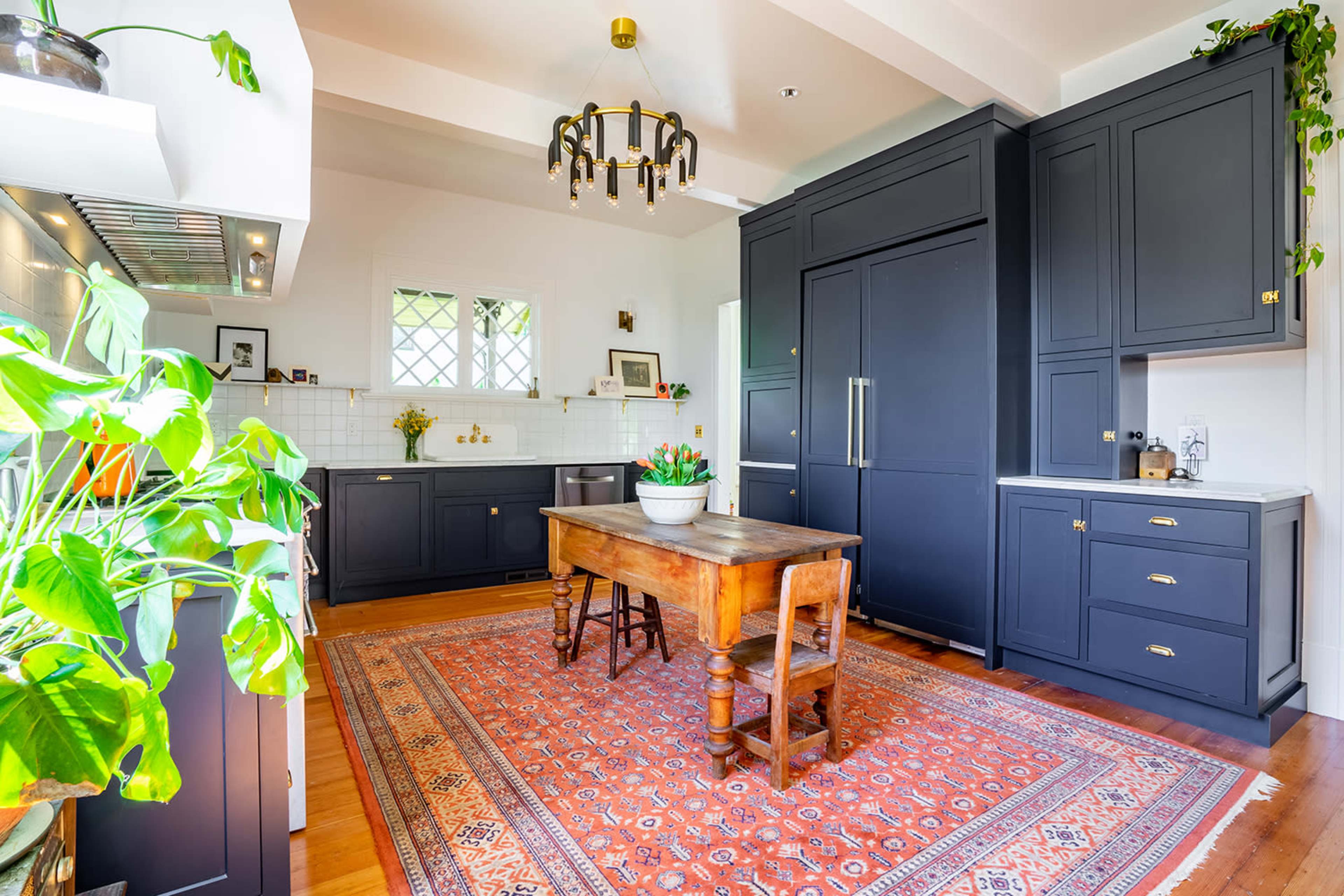 A modern kitchen features dark cabinetry, a wooden dining table surrounded by chairs, and a patterned area rug.