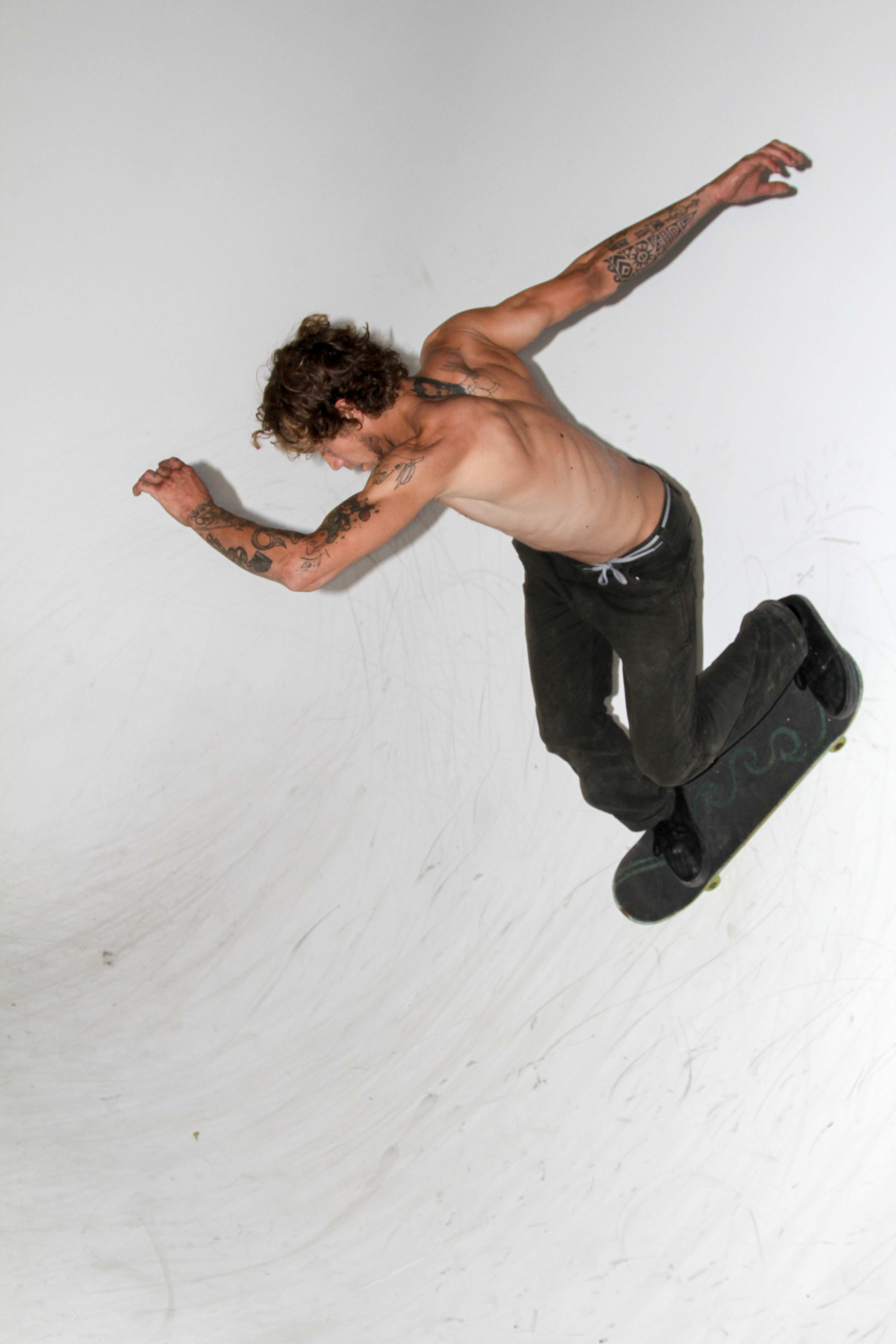 A shirtless skateboarder performs a trick in a half-pipe.
