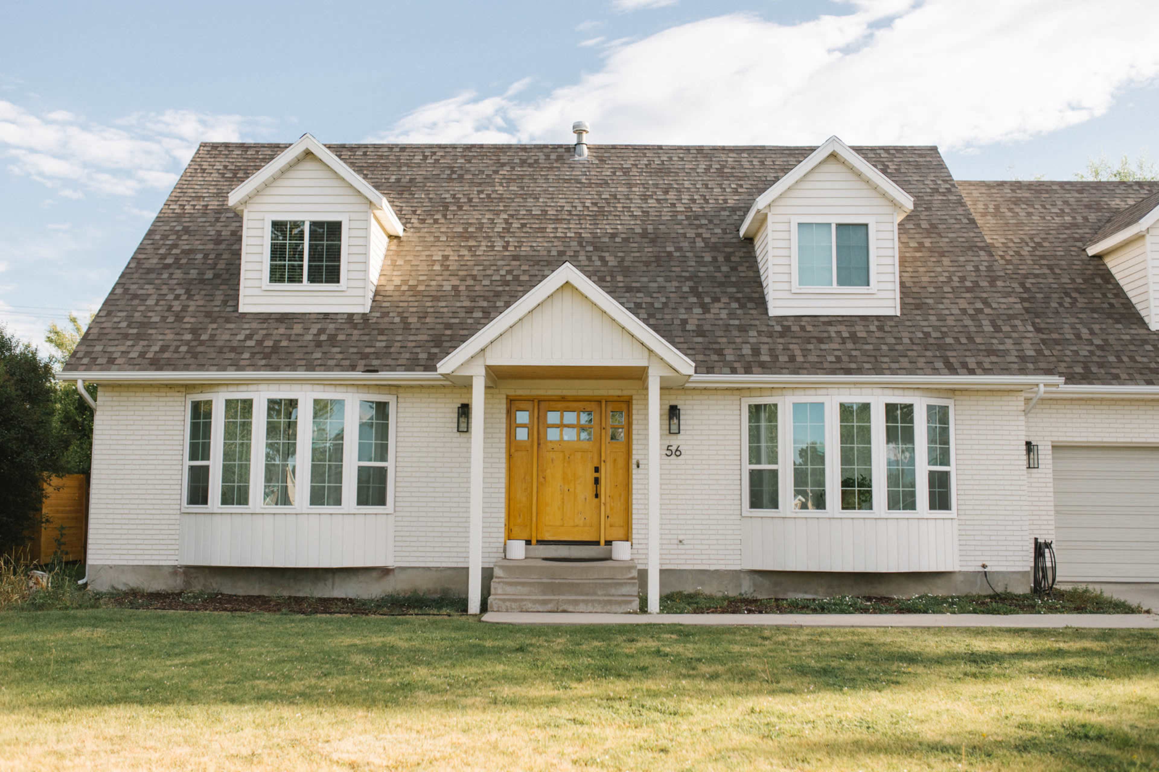 The image shows a two-story house with a light-colored exterior, a pitched roof, and a wooden front door.