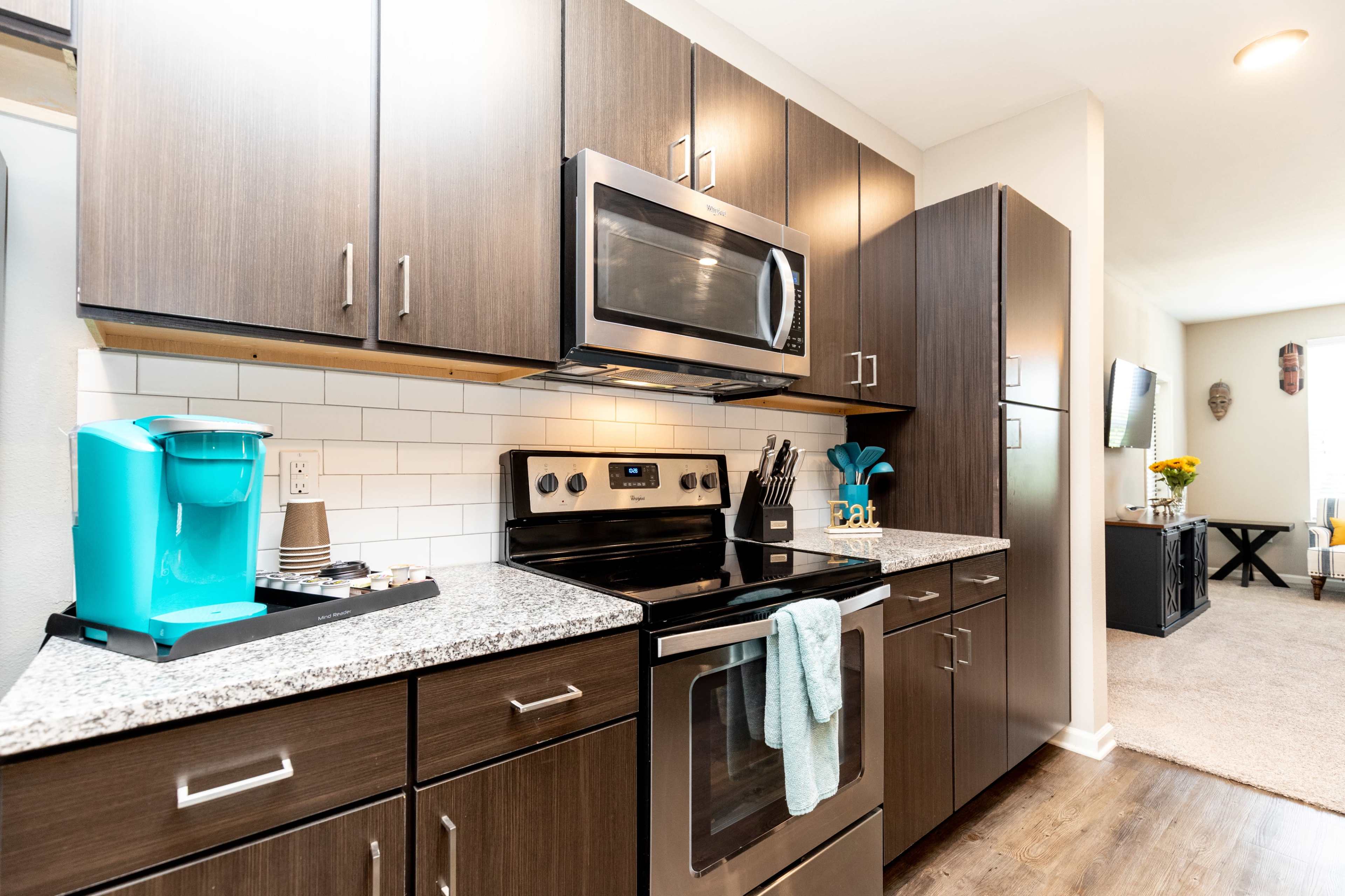 A modern kitchen features dark wood cabinets, stainless steel appliances, and a white tiled backsplash with a granite countertop.