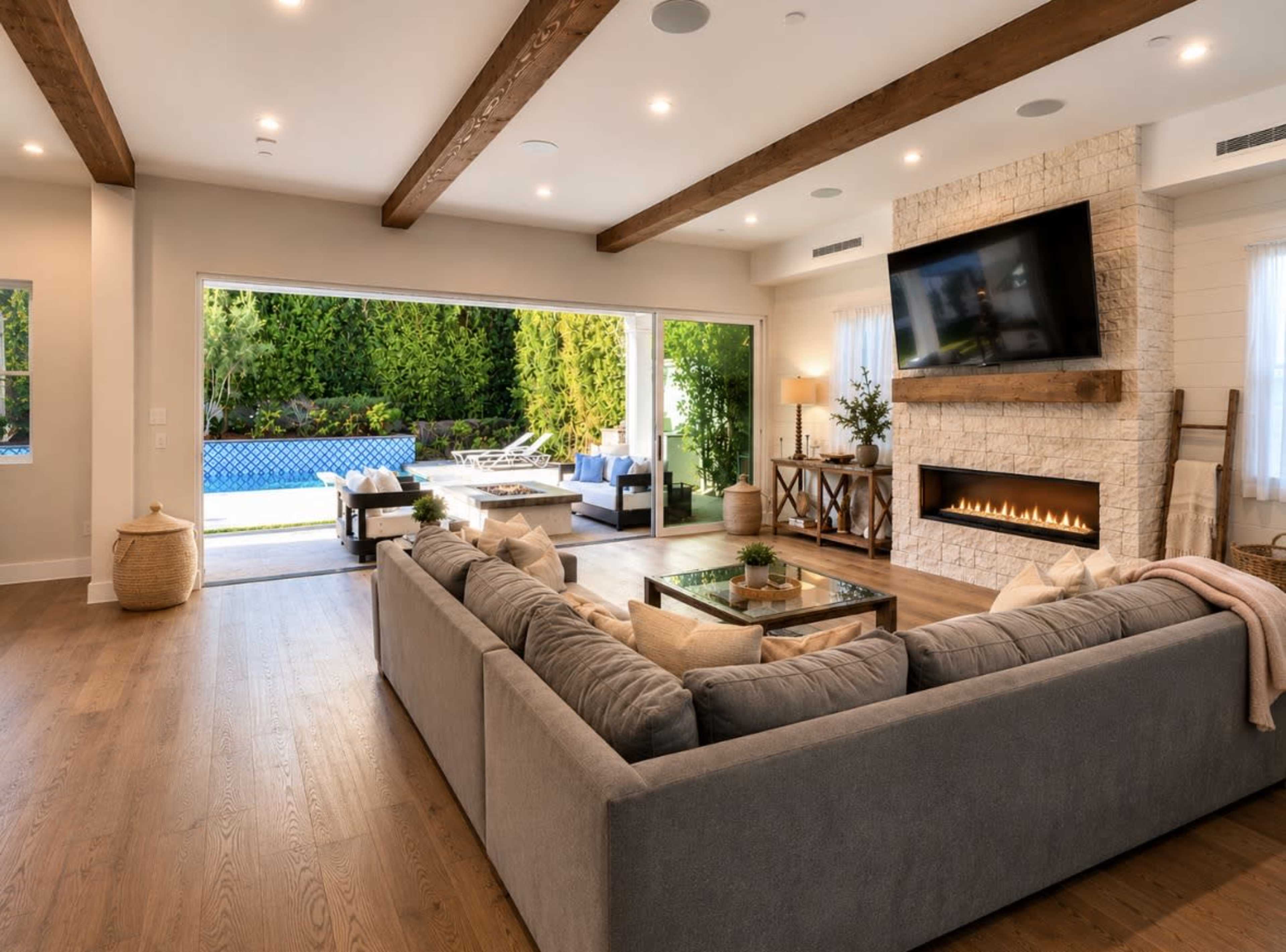 The open living room features a large gray sectional sofa facing a modern fireplace and a sliding glass door that overlooks a pool area with outdoor seating.